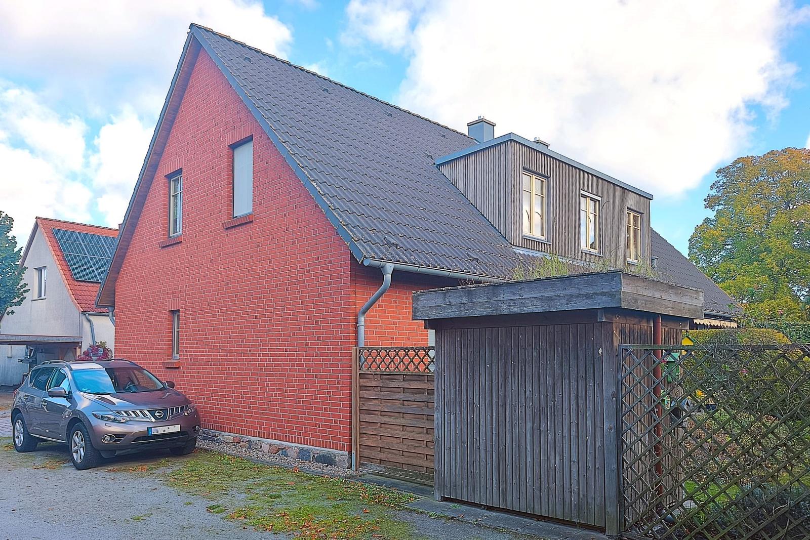 Rotes Backsteinhaus mit Dachgeschoss und Holzgarage. Auto parkiert vor dem Haus.