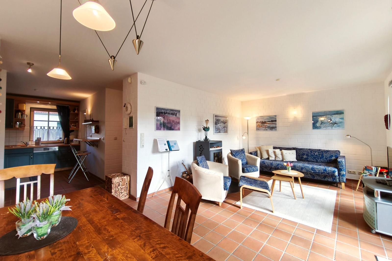 Wohn- und Essbereich mit Küche. Wohnzimmer mit Sofa und Sessel. Terrakottaboden und weiße Wände.