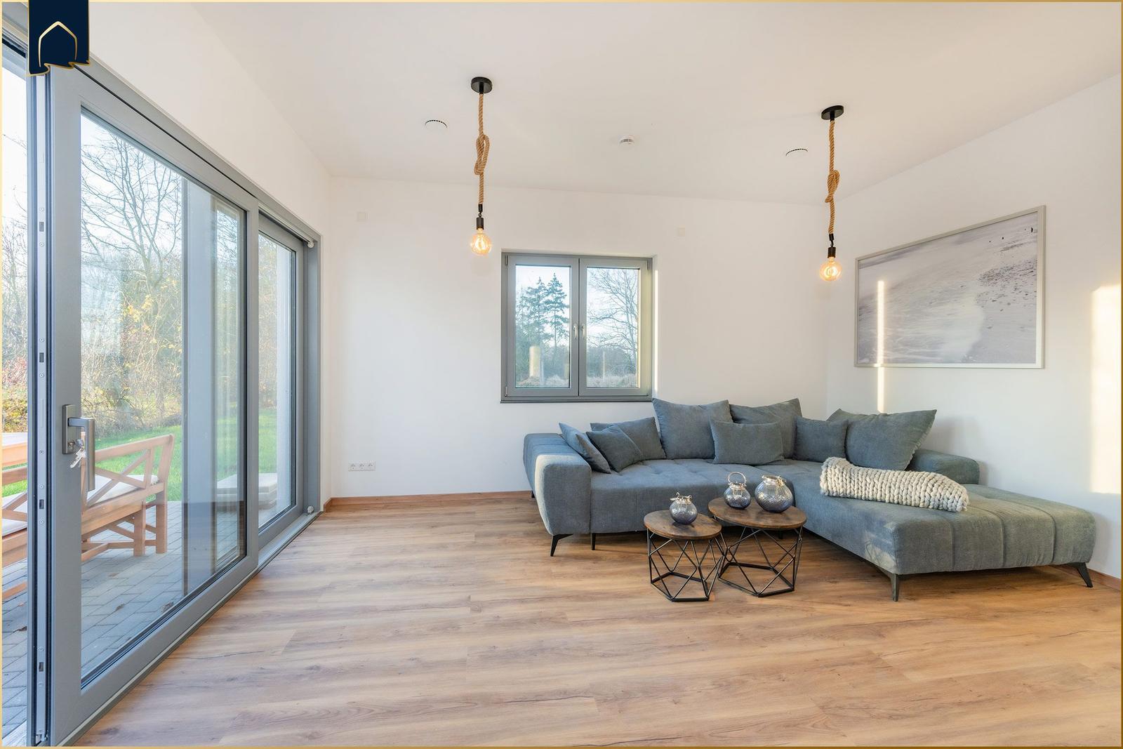 Wohnzimmer mit grauem Sofa, Holzboden und großem Fensterfront zur Terrasse.