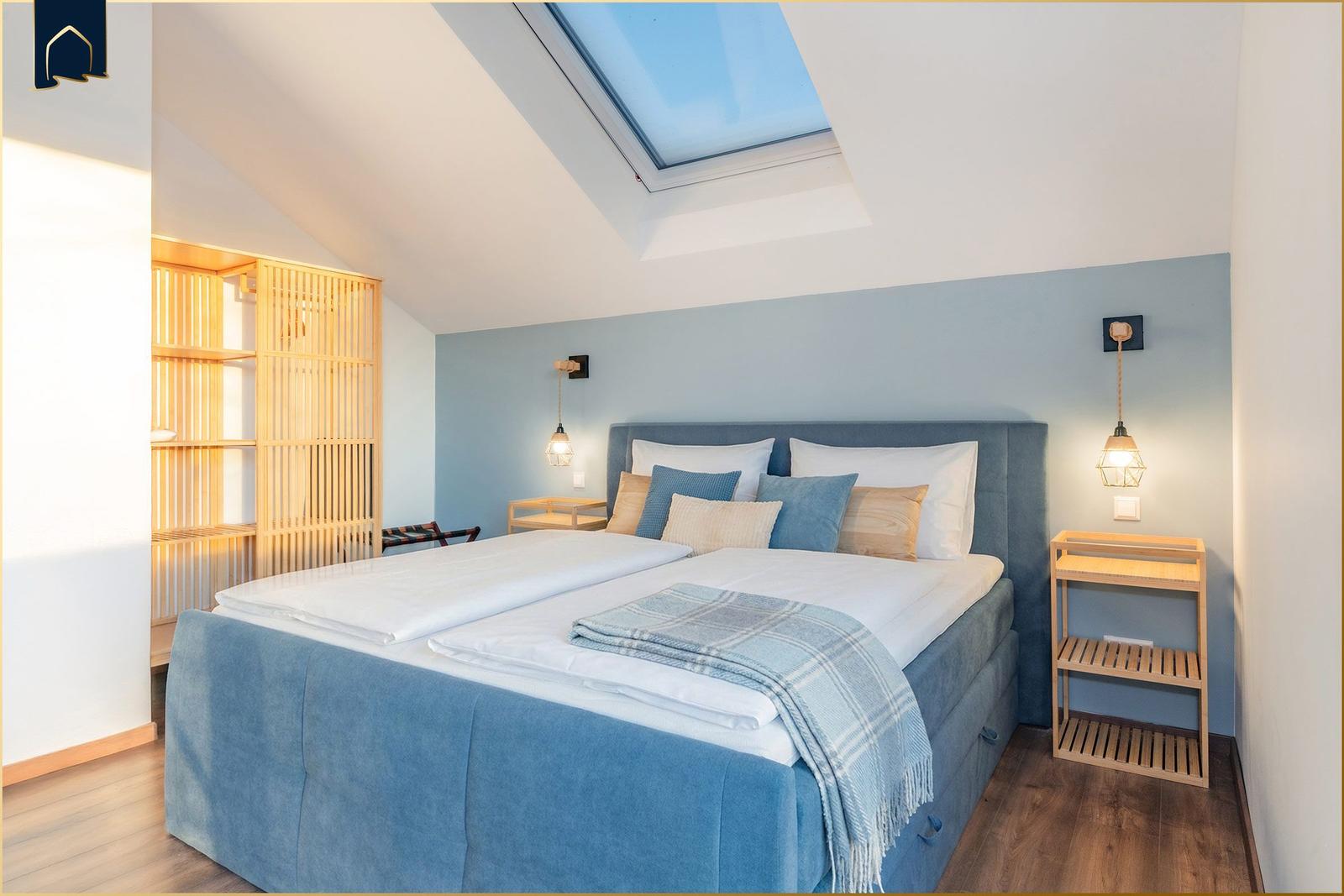 Schlafzimmer mit Dachfenster, Bett und Holzmöbel.