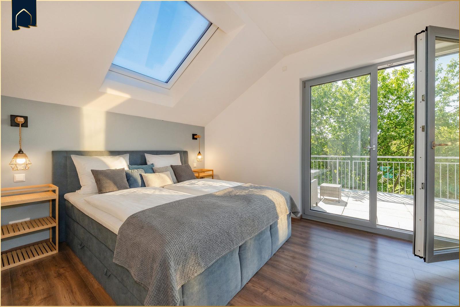 Schlafzimmer mit Dachfenster und Balkon. Bett, Nachttische und Holzregal.
