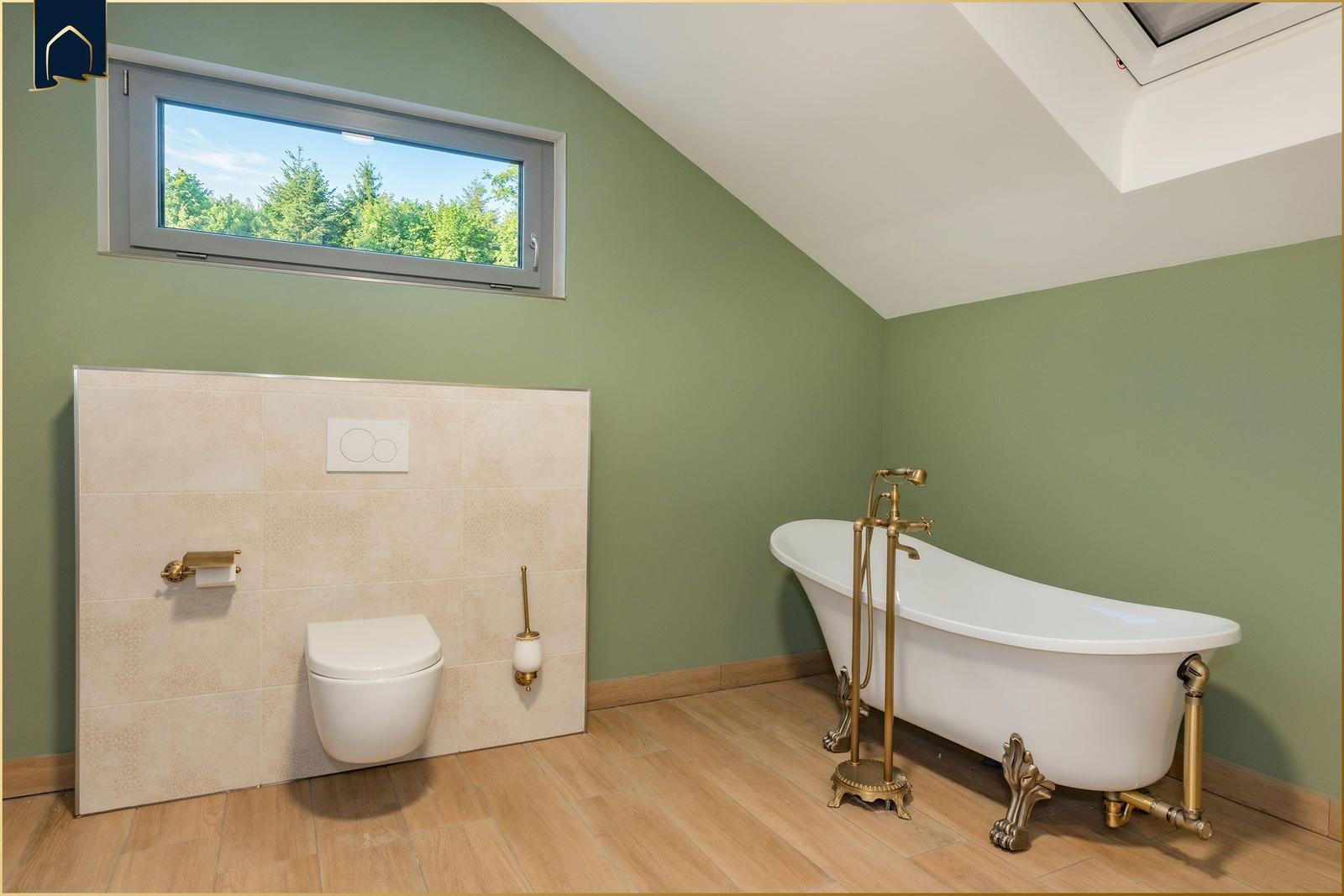 Badezimmer mit freistehender Badewanne, WC und Dachfenster mit Blick auf Wald.
