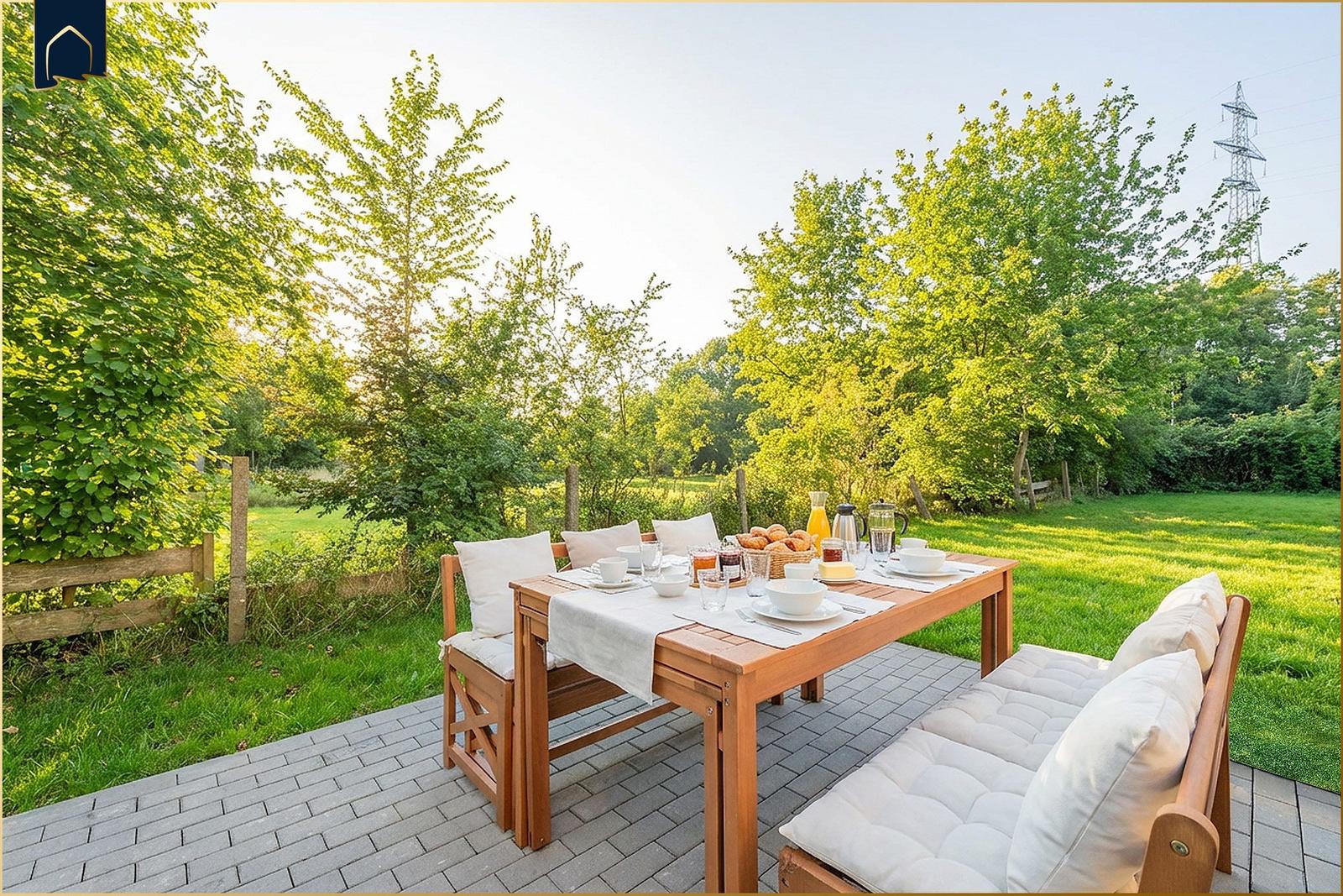 Terrasse mit Holztisch und Sitzgelegenheiten, umgeben von Grün und Bäumen.