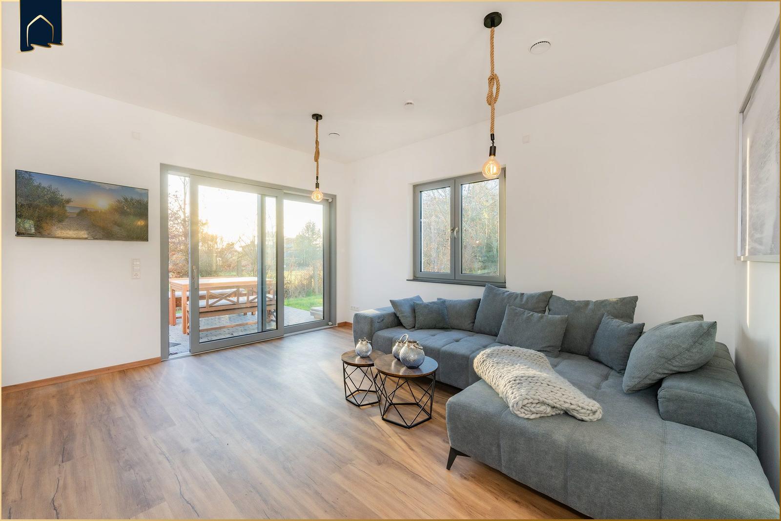 Wohnzimmer mit grauem Sofa, Holzboden und Glas-Tür zur Terrasse.