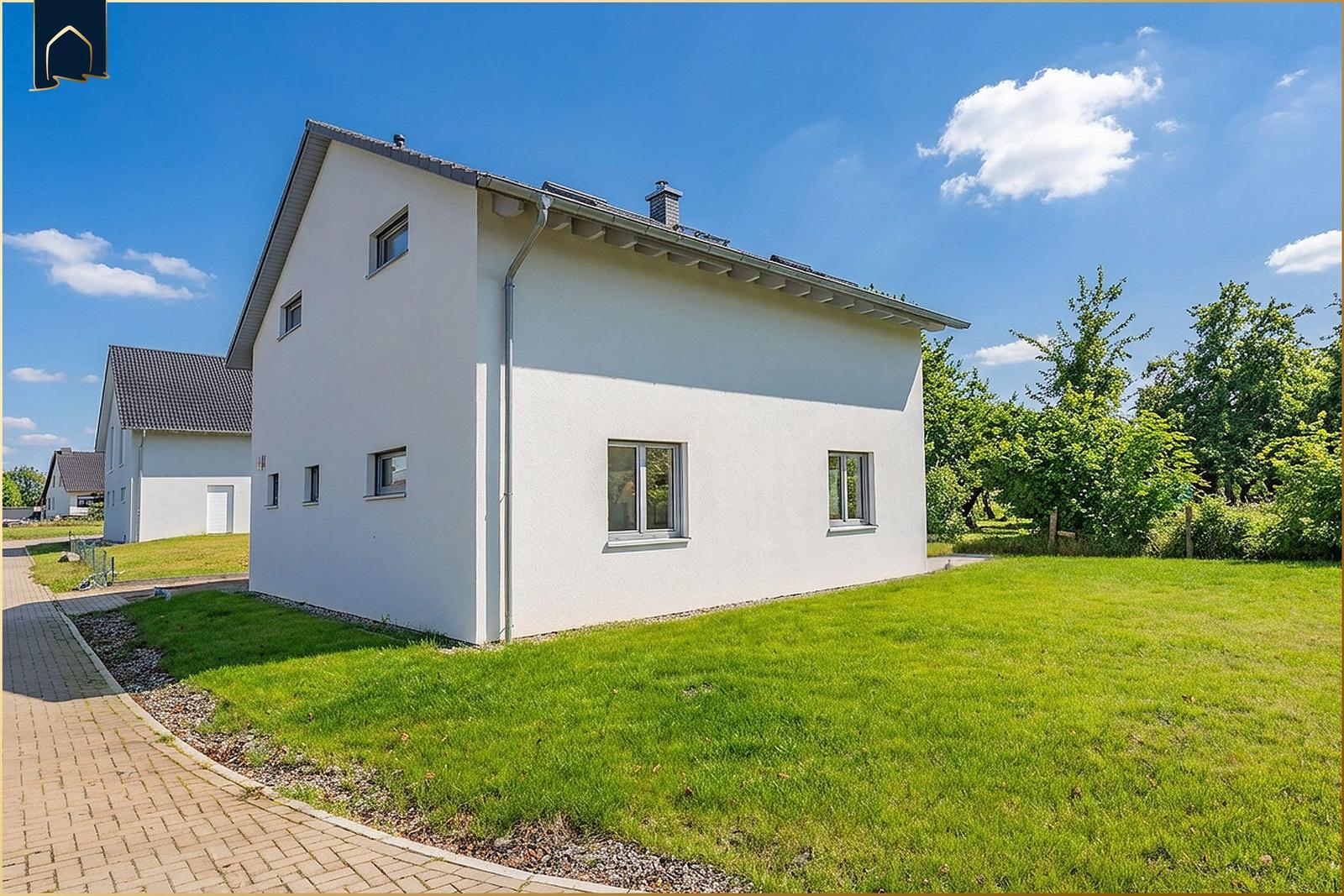 Moderne weiße Villa mit grünem Rasen und Bäumen im Hintergrund.