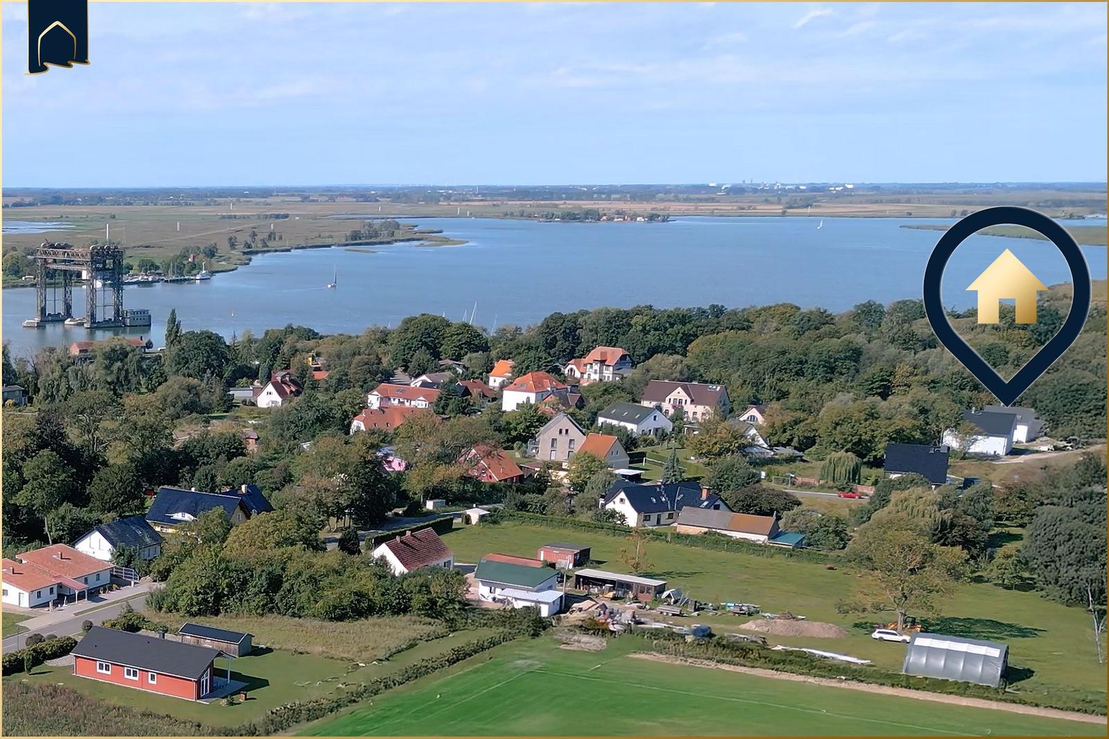 Luftbild eines Dorfes am Wasser mit Häusern und Grünflächen.