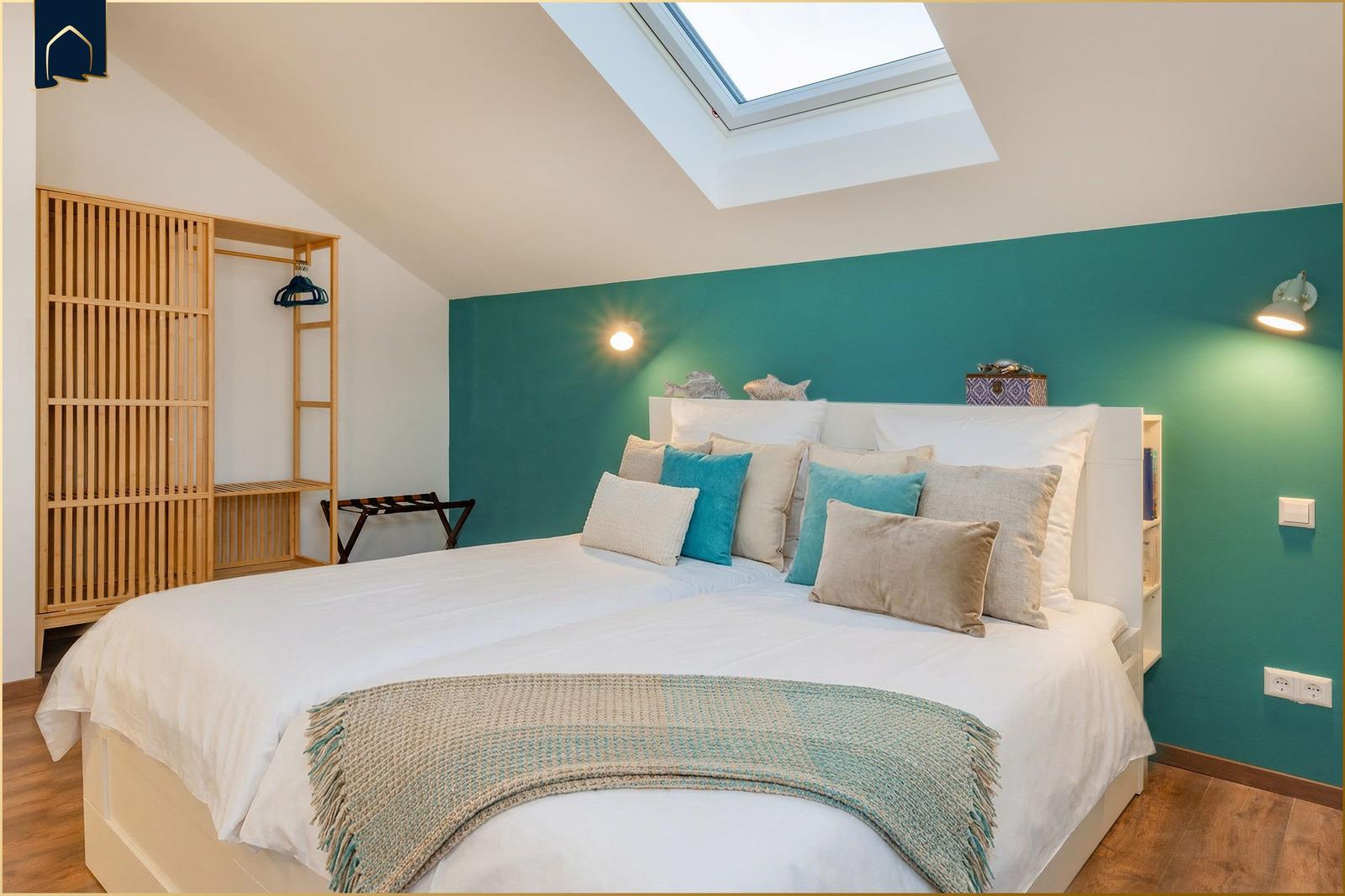 Schlafzimmer mit Dachschrägen, grüner Wand und Dachfenster. Bett mit Kissen und Decke.