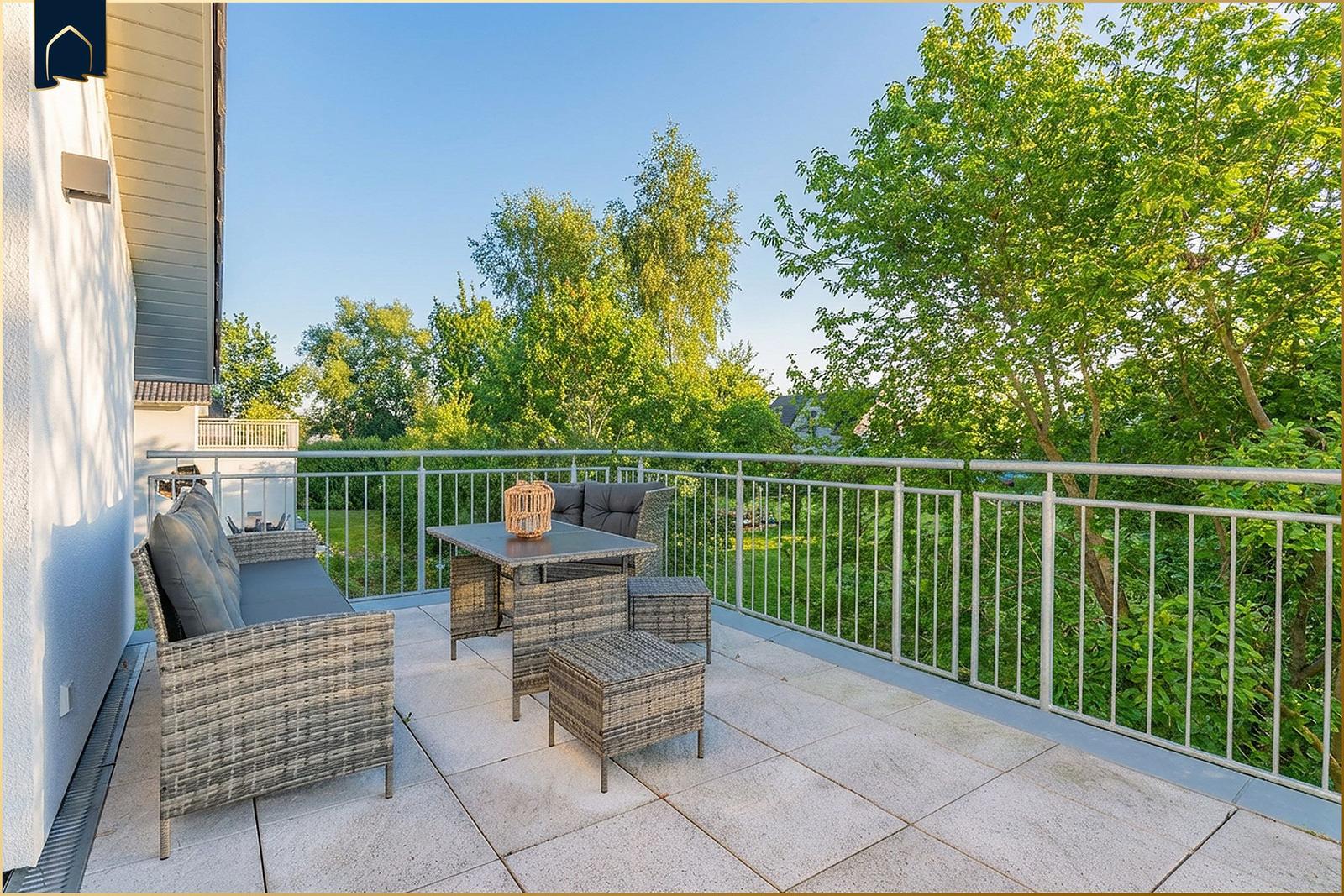 Terrasse mit Sitzgruppe und Tisch. Blick auf grüne Bäume und Garten.