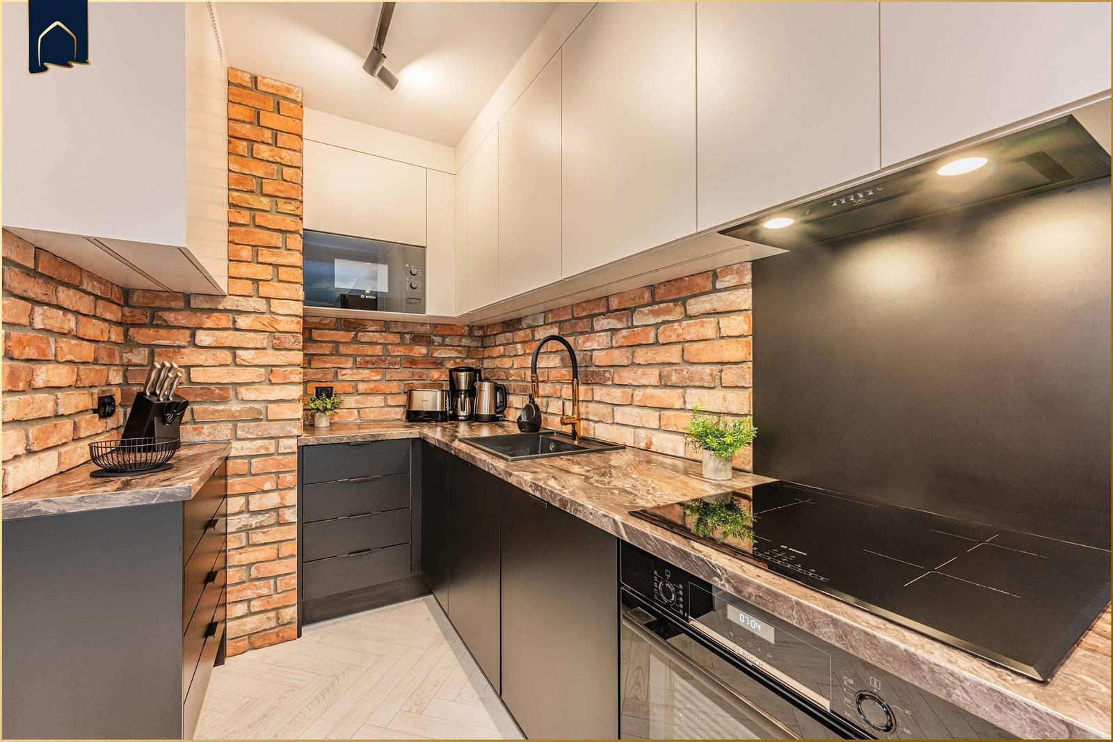 Küche mit Backsteinwand, Edelstahlspüle und Kochfeld