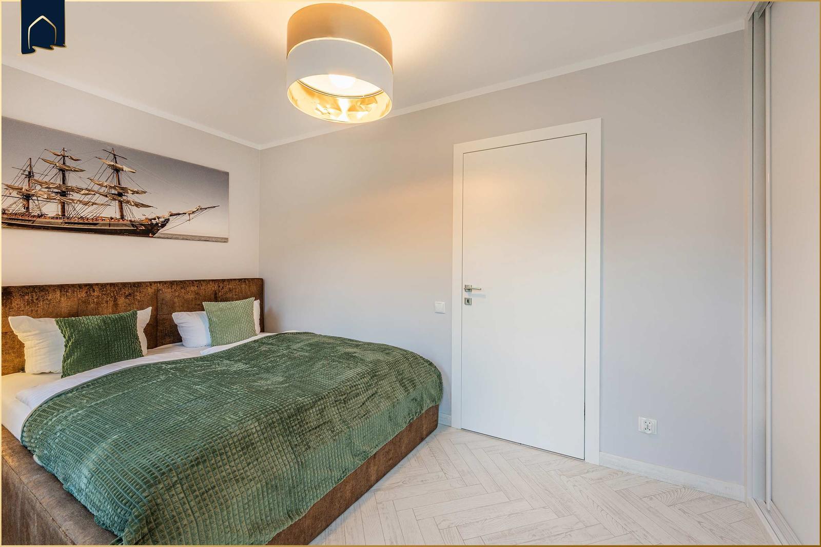 Schlafzimmer mit Bett, Wandbild und Deckenleuchte.