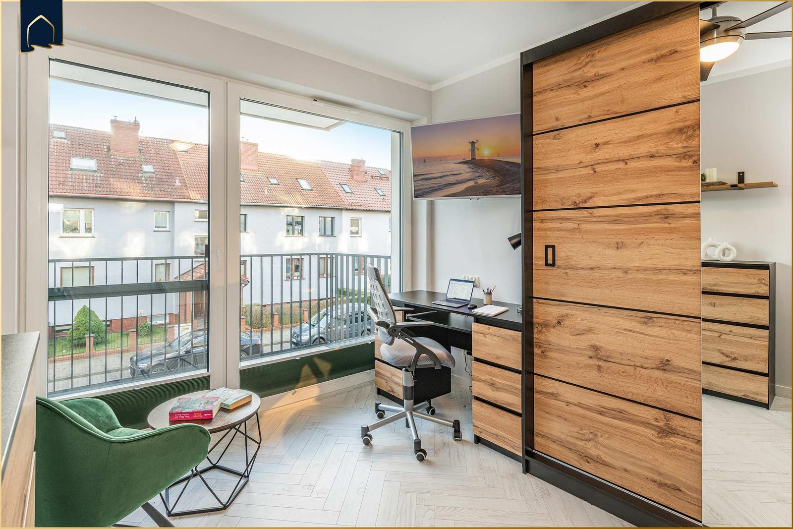 Schlafzimmer mit Schreibtisch, grüner Sessel und Balkonansicht