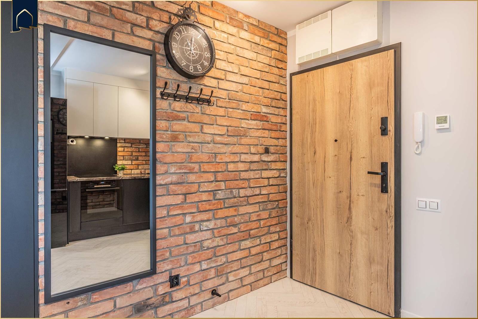Eingangsbereich mit Holztür, Backsteinwand und Blick in die Küche.
