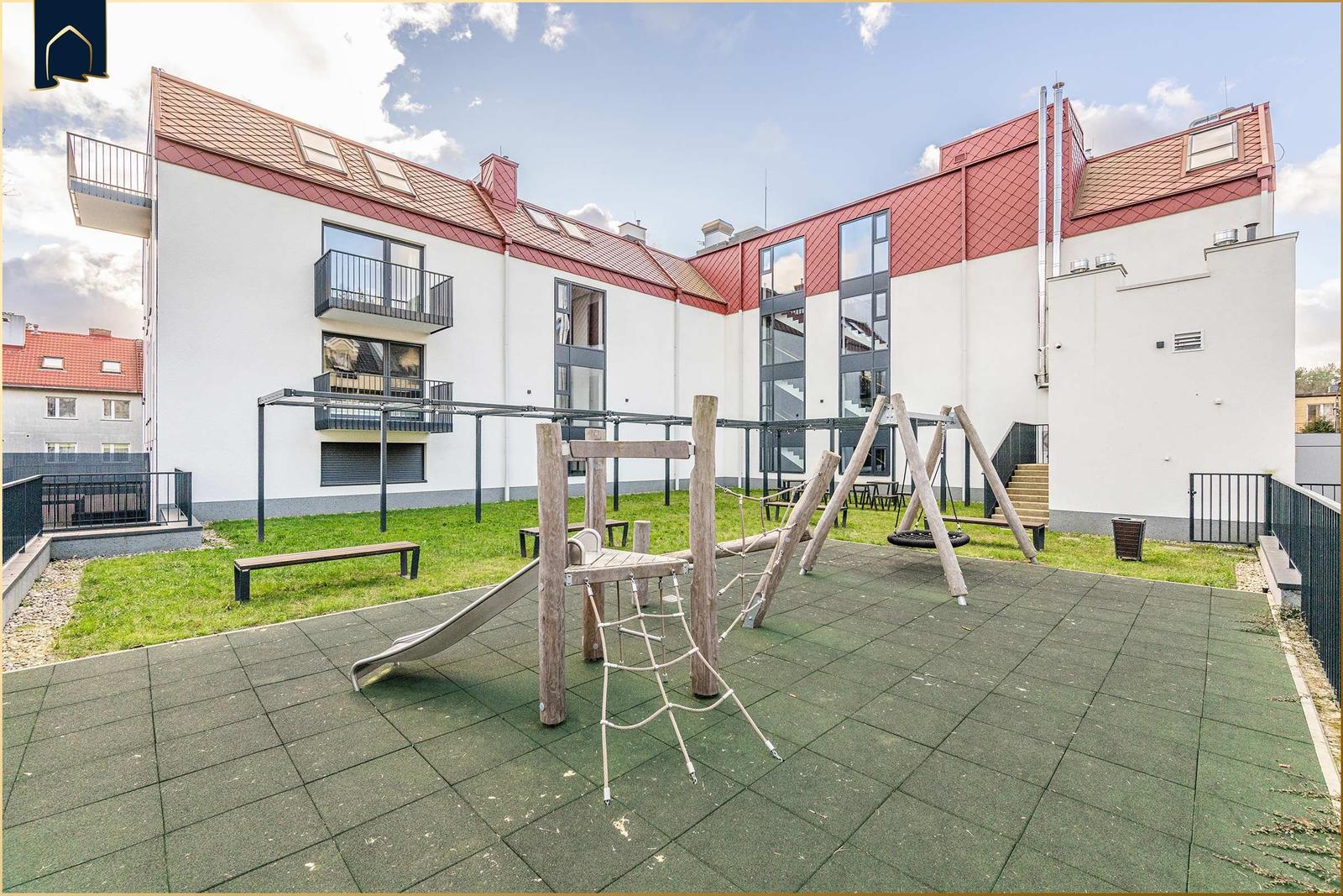 Hinterhof mit Spielplatz, Grünfläche und modernem Gebäude mit Balkonen.