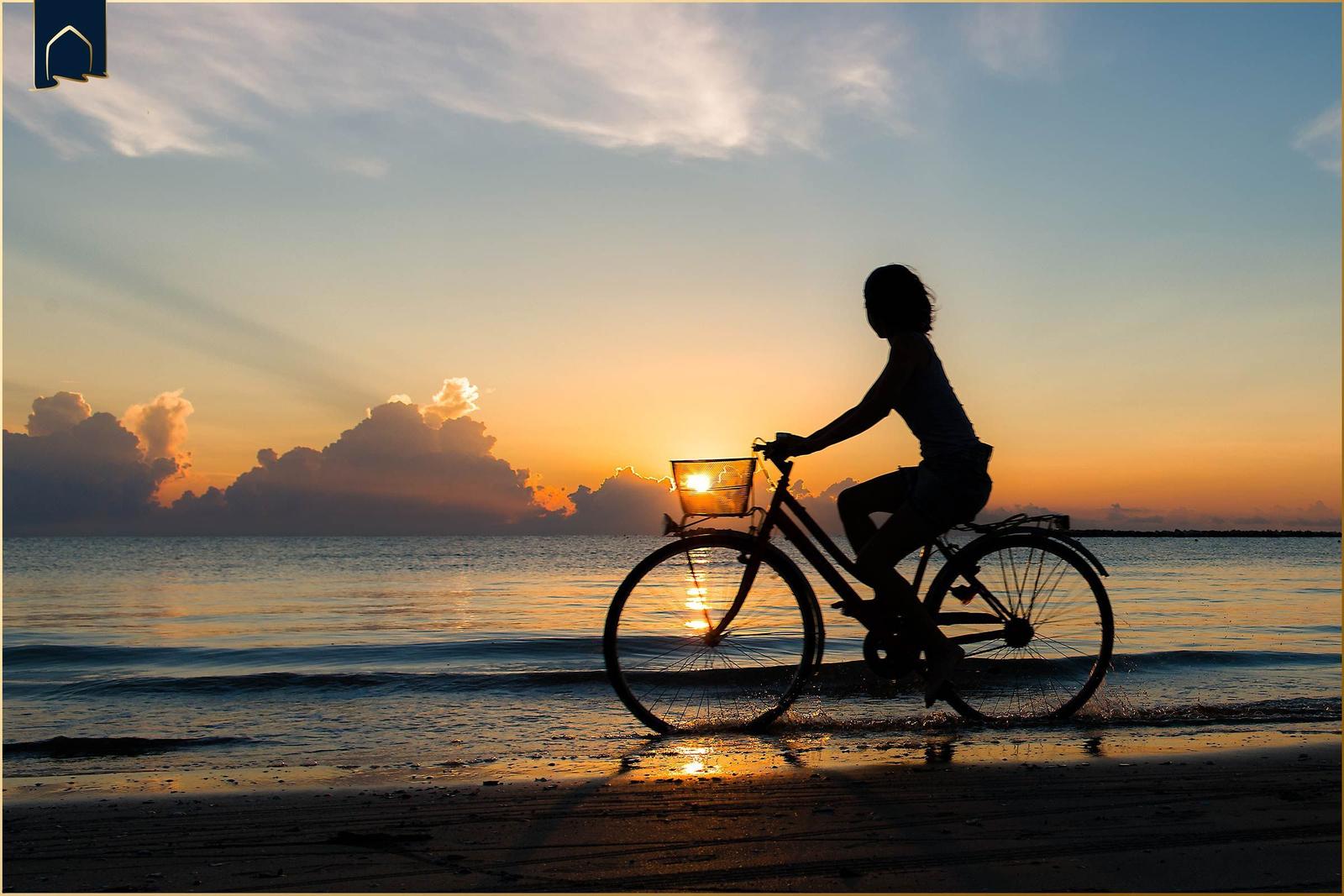 Silhouette einer Person, die ein Fahrrad am Strand bei Sonnenuntergang fährt.