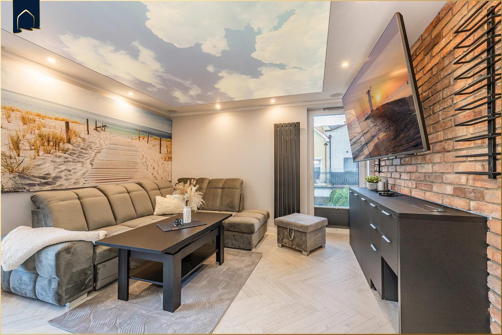 Wohnzimmer mit Sofa, Couchtisch und Fernseher an Backsteinwand.