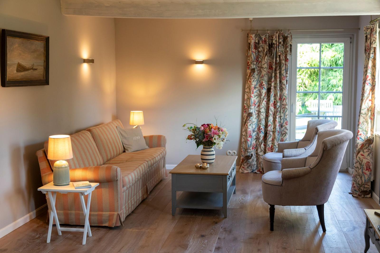 Wohnzimmer mit Sofa, zwei Sesseln, Tisch und Fenster zur Terrasse.