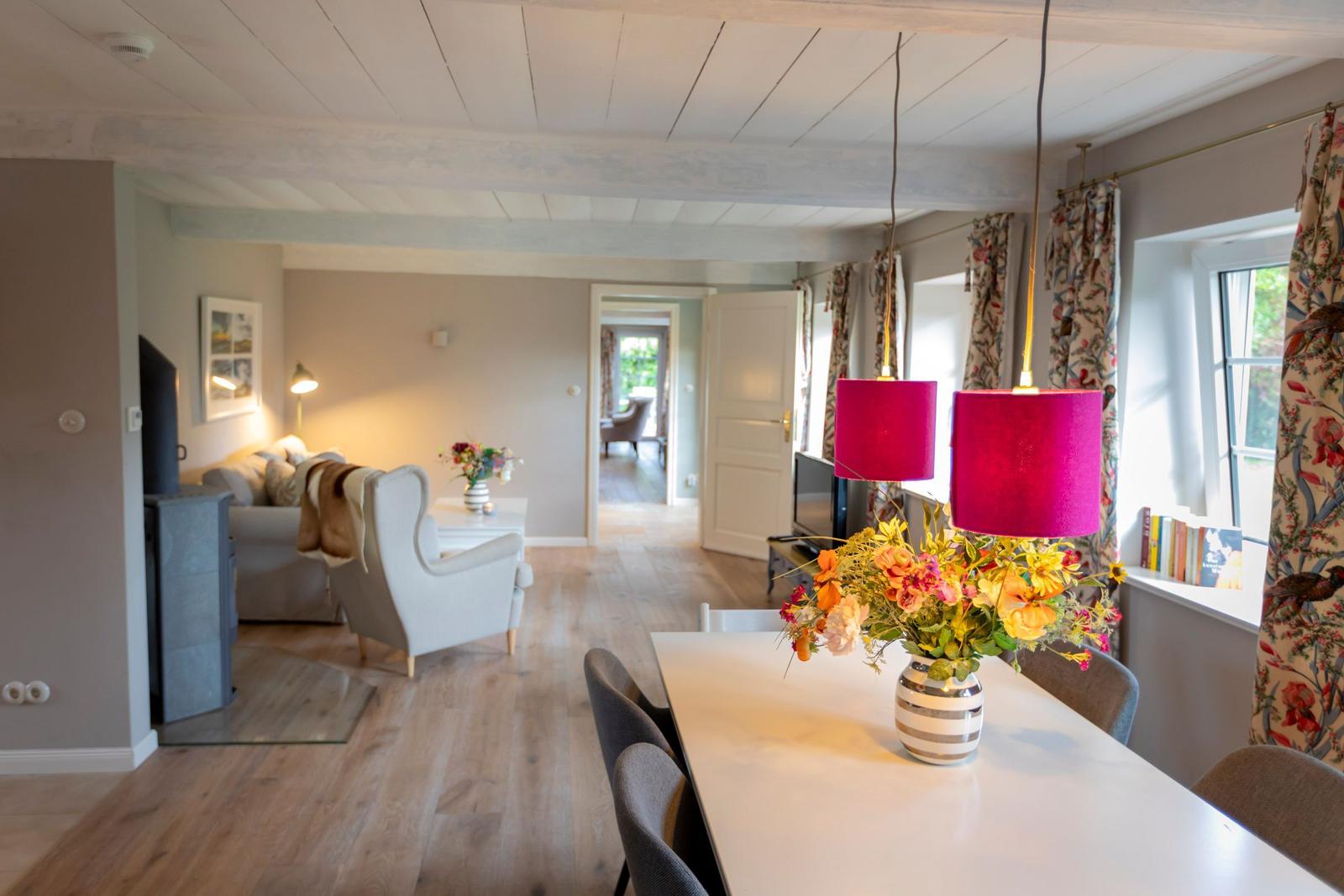 Essbereich mit Tisch, Stühlen und Blumen. Wohnzimmer mit Sofa, Sessel und Fernseher.