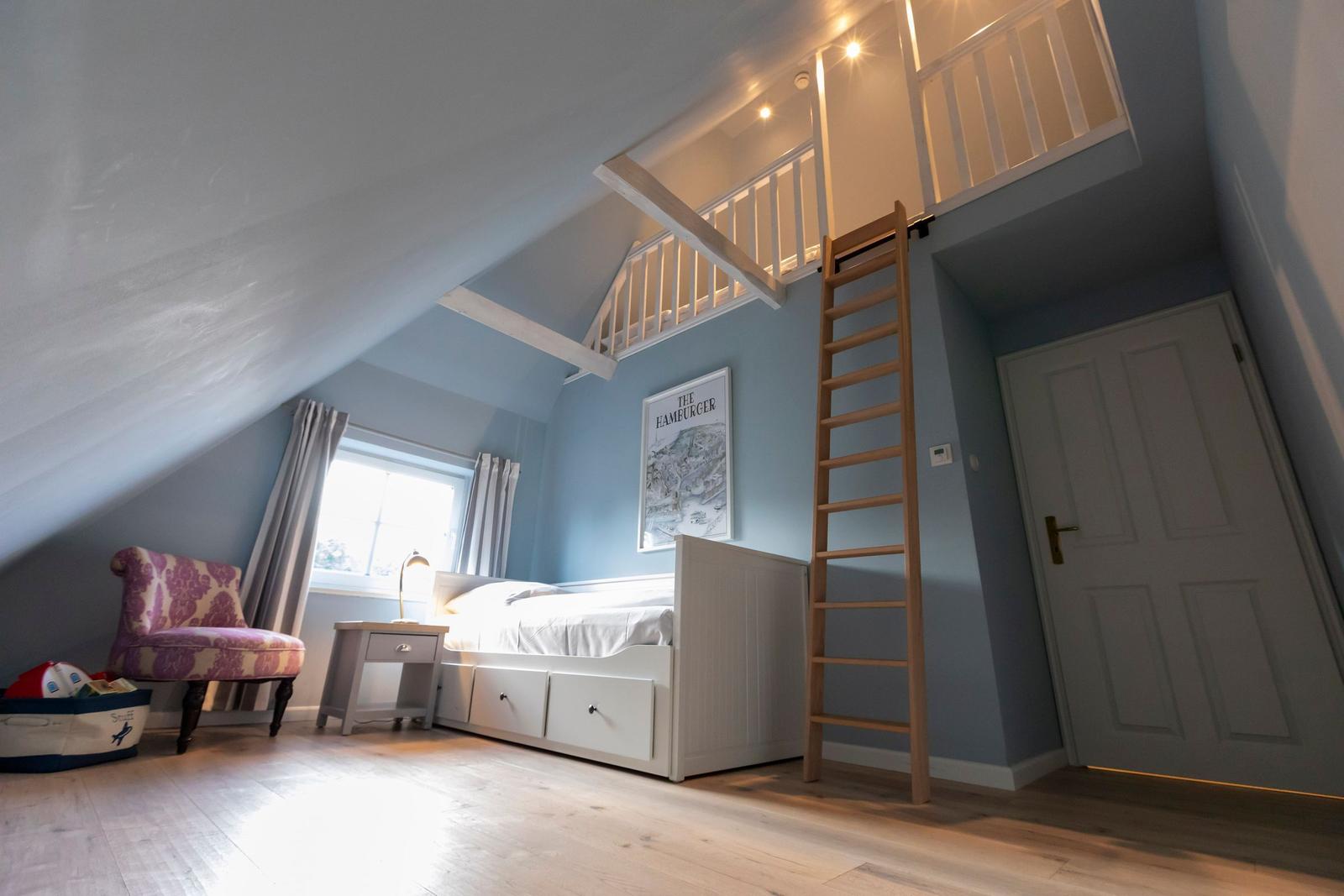 Schlafzimmer mit Dachschrägen, Bett, Leiter und Fenster.