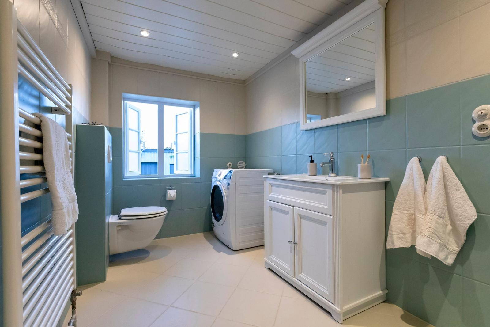 Badezimmer mit Waschmaschine, Toilette und Spiegelschrank.