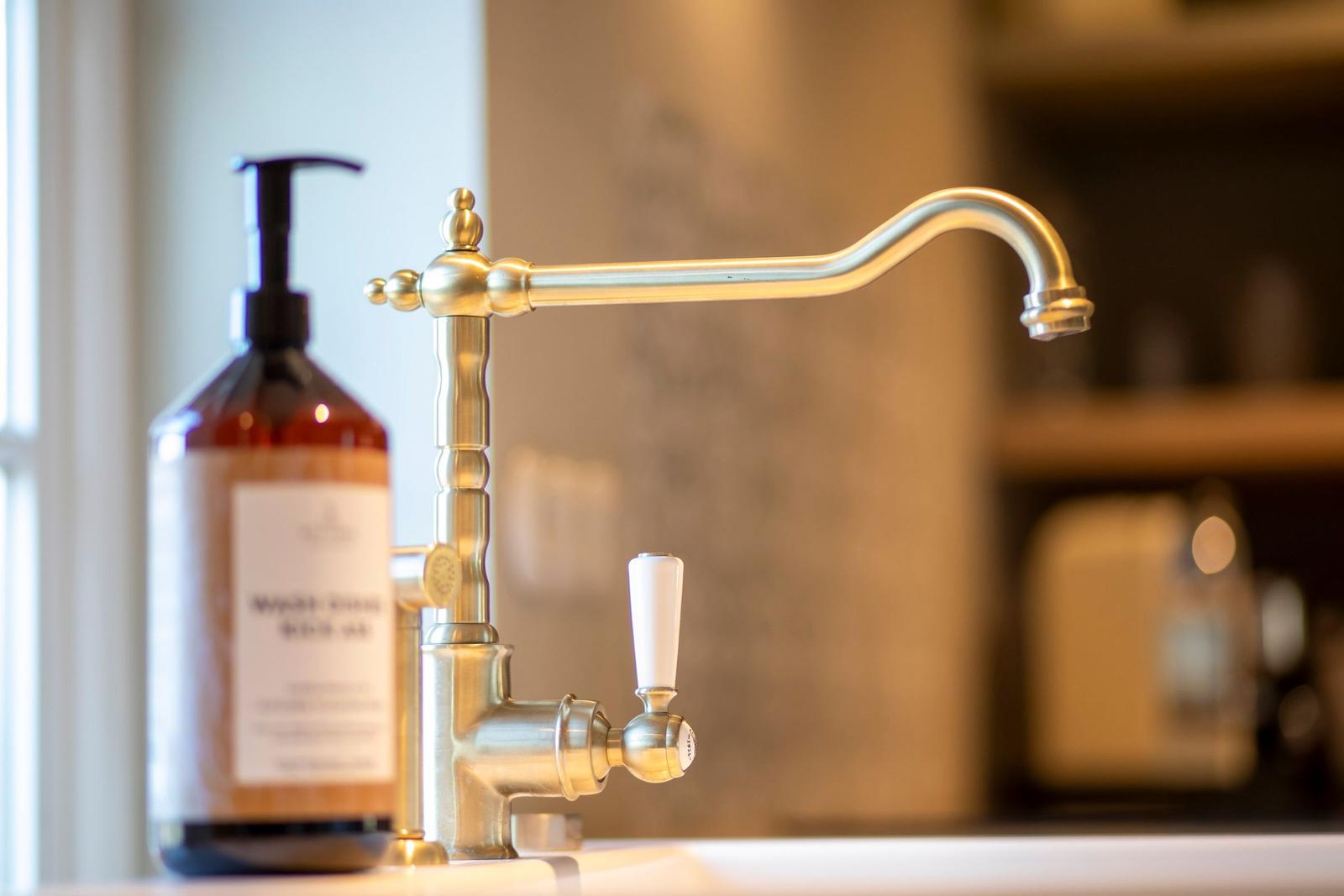 Edler Wasserhahn mit Drehkurbel und Seifenspender auf Küchenarbeitsfläche.