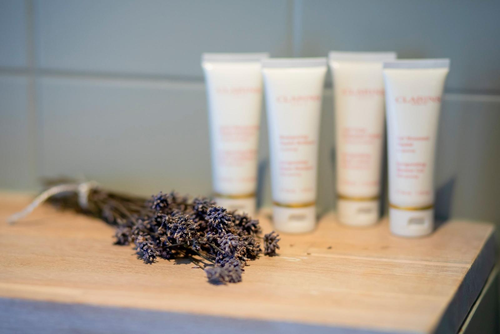 Draufsicht auf Lavendel und vier weiße Creme-Fläschchen auf Holzoberfläche.