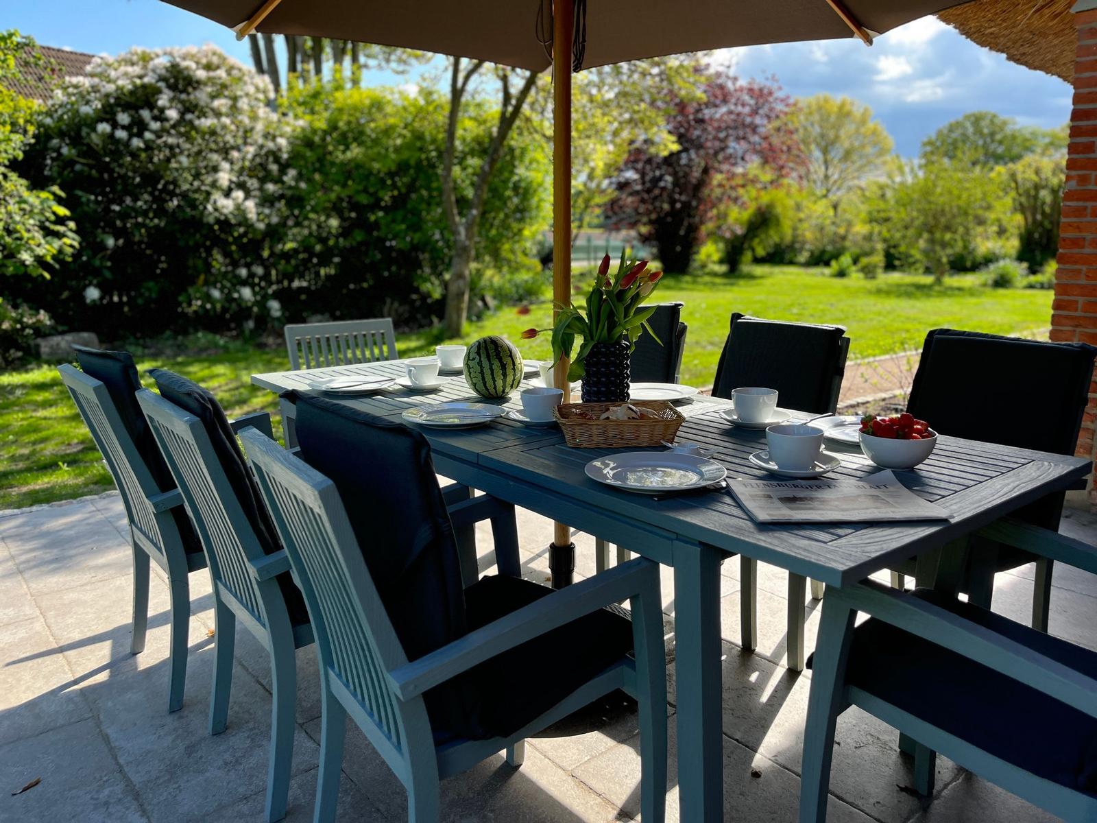 Garten-Tisch mit Stühlen, Sonnenschutz, Obst und Zeitung auf dem Platz.