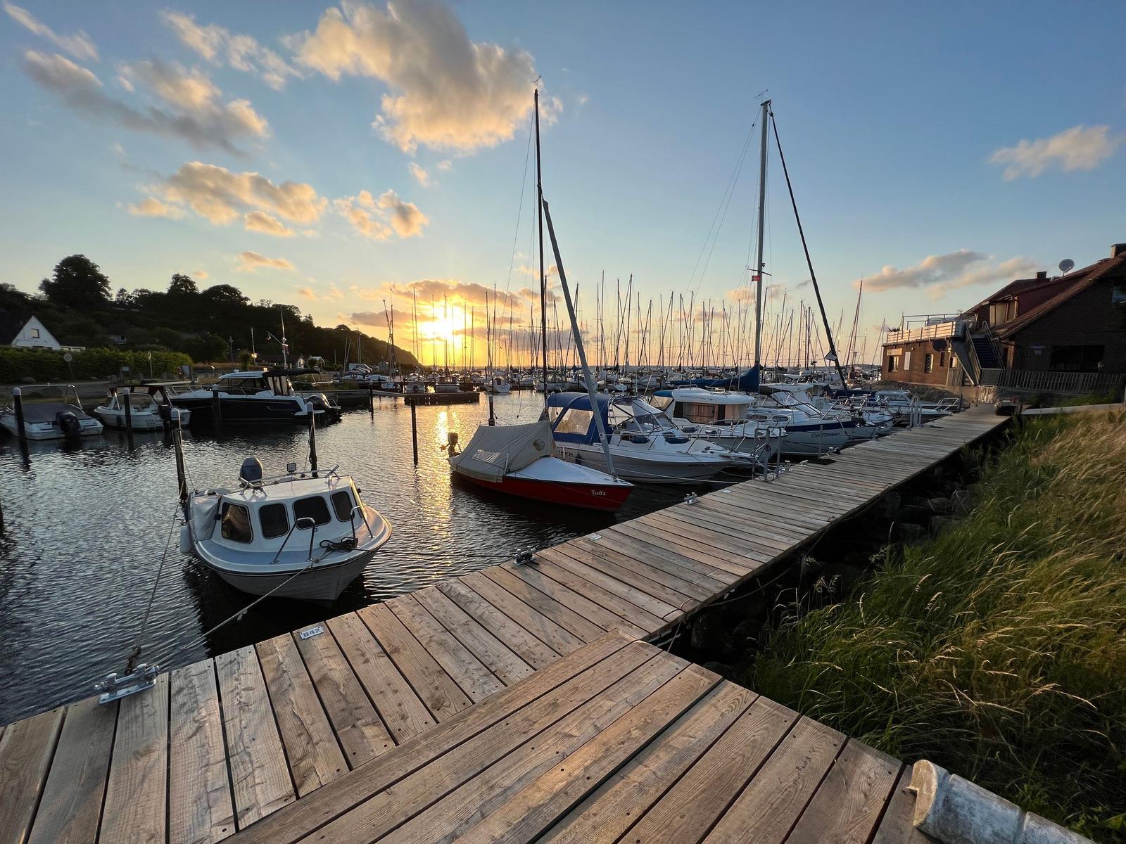 Hafen mit Booten und Holzsteg bei Sonnenuntergang.