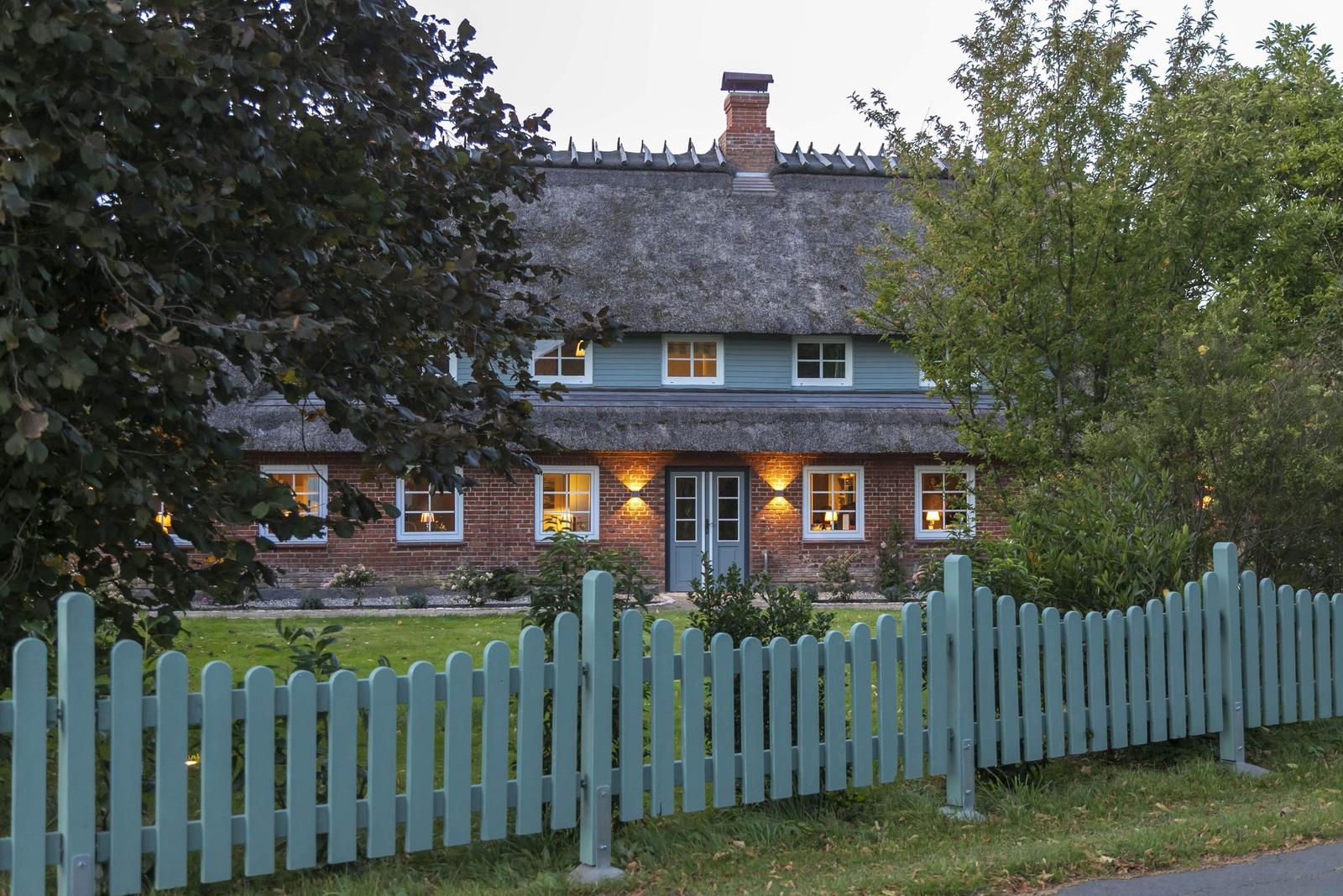 Ein Haus mit strohgedecktem Dach, rotem Backstein und hellblauem Zaun.