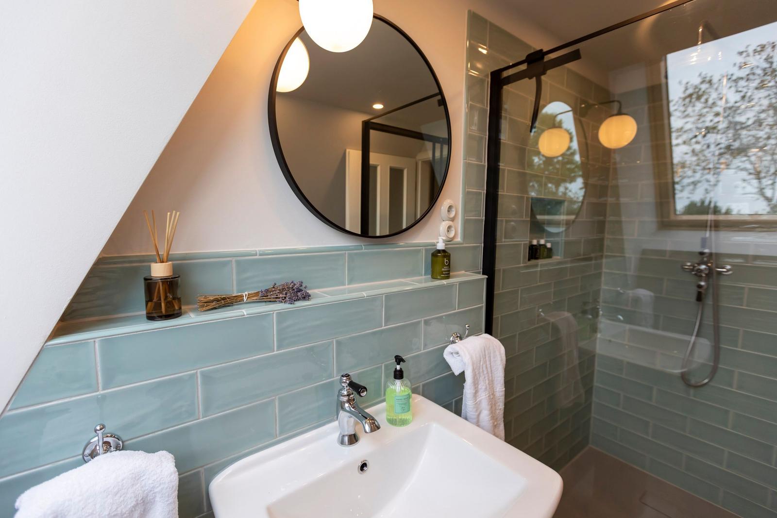Bad mit Waschbecken, Dusche und Spiegel. Wandfliesen in Hellblau.