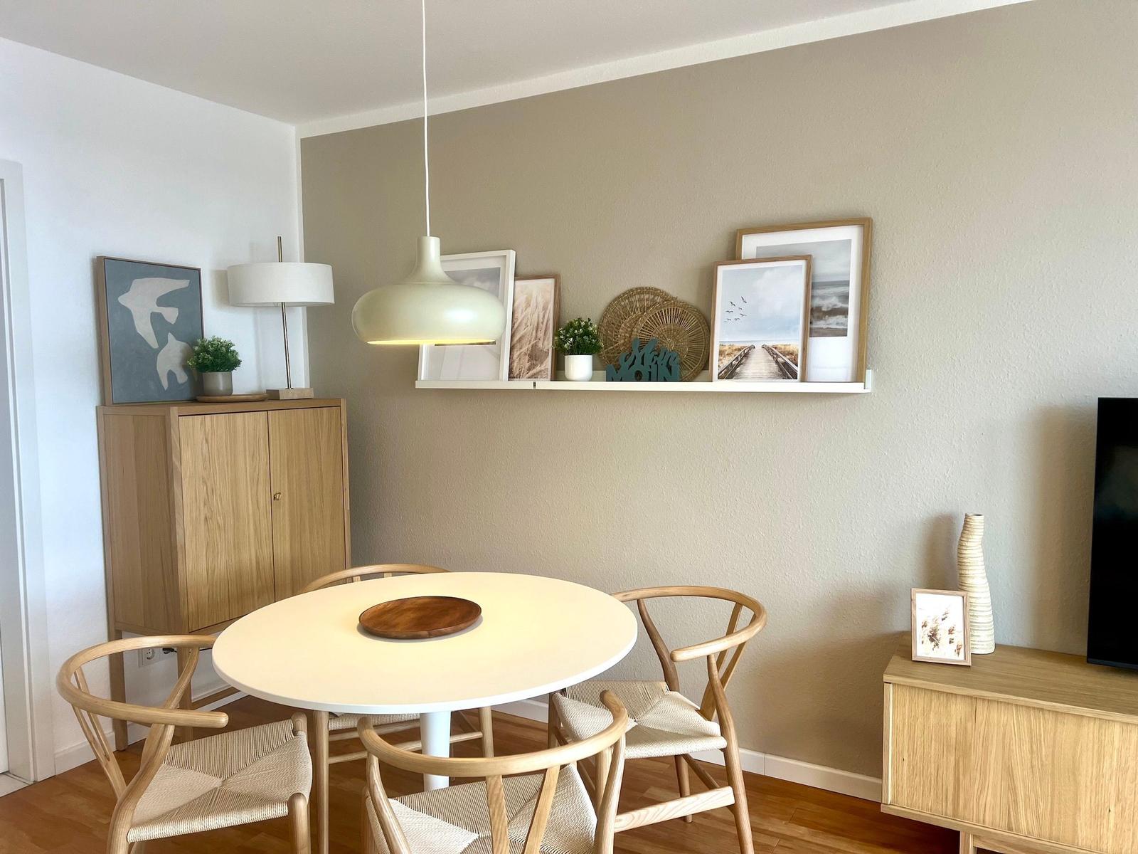 Runder Tisch mit vier Stühlen, Wandregal mit Bildern und Lampe.