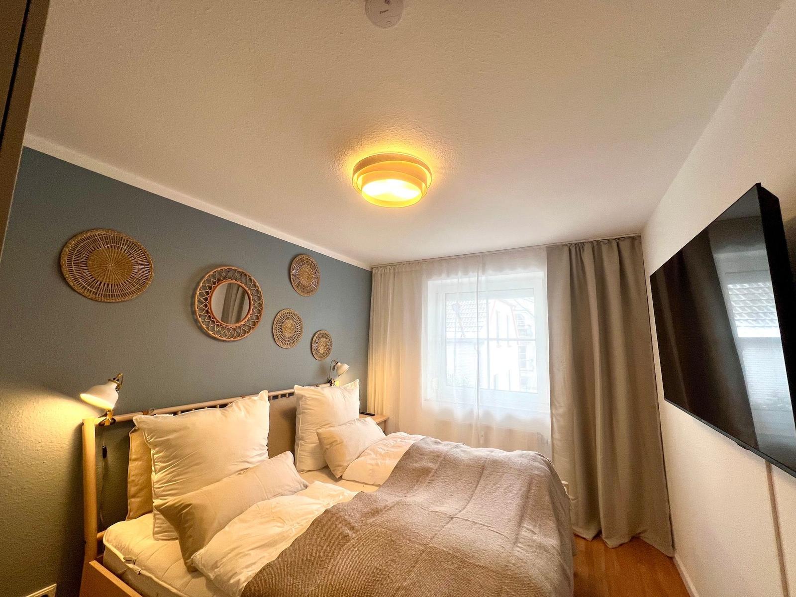 Schlafzimmer mit Bett, Fenster, TV und Wanddekoration.