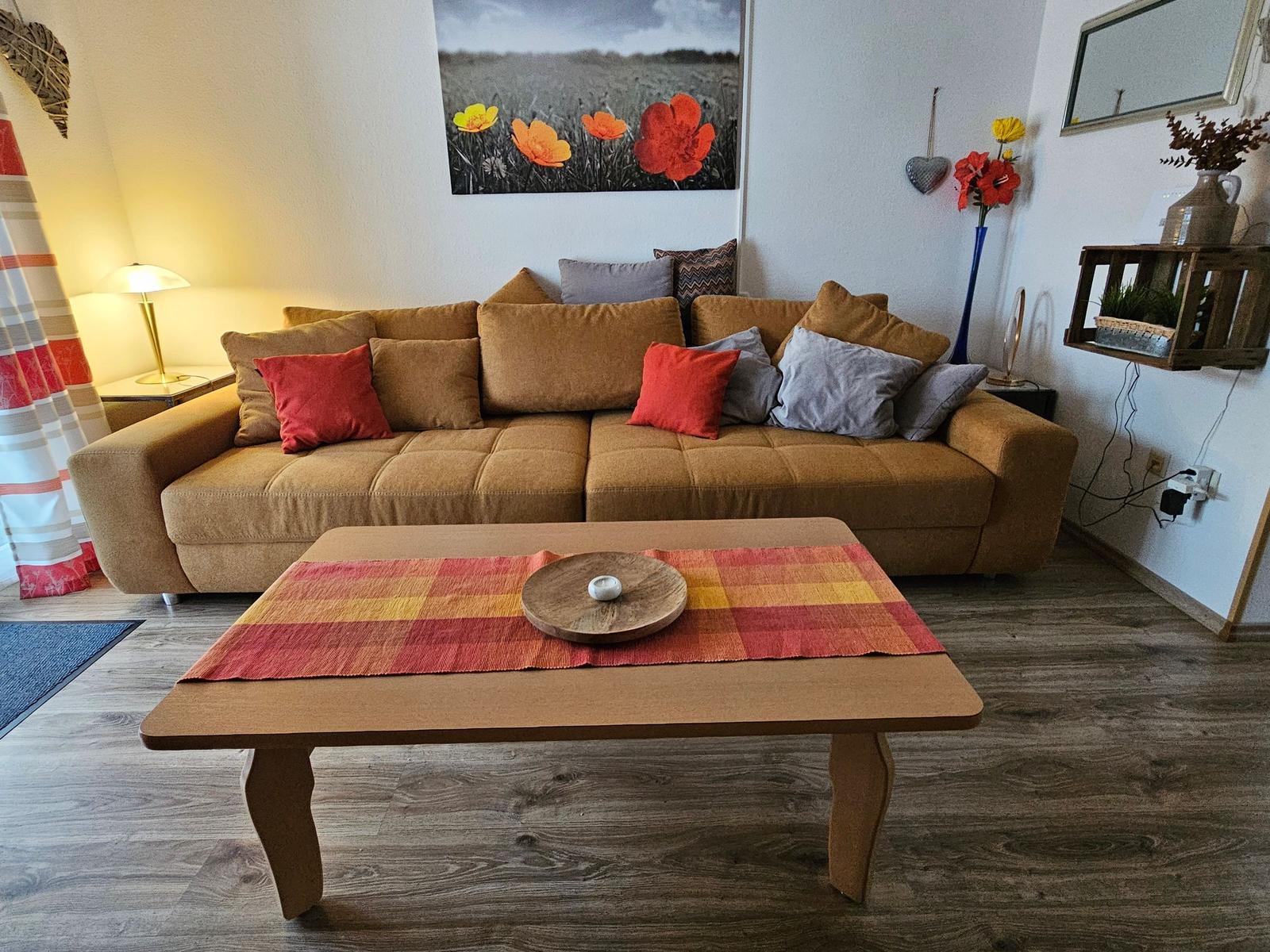 Ein Wohnzimmer mit braunem Sofa, Holztisch und Wandbild mit Blumen.