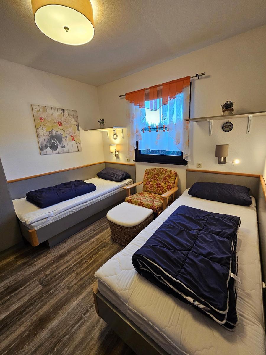 Zwei Einzelbetten, ein Sessel und ein Fenster mit Vorhängen.