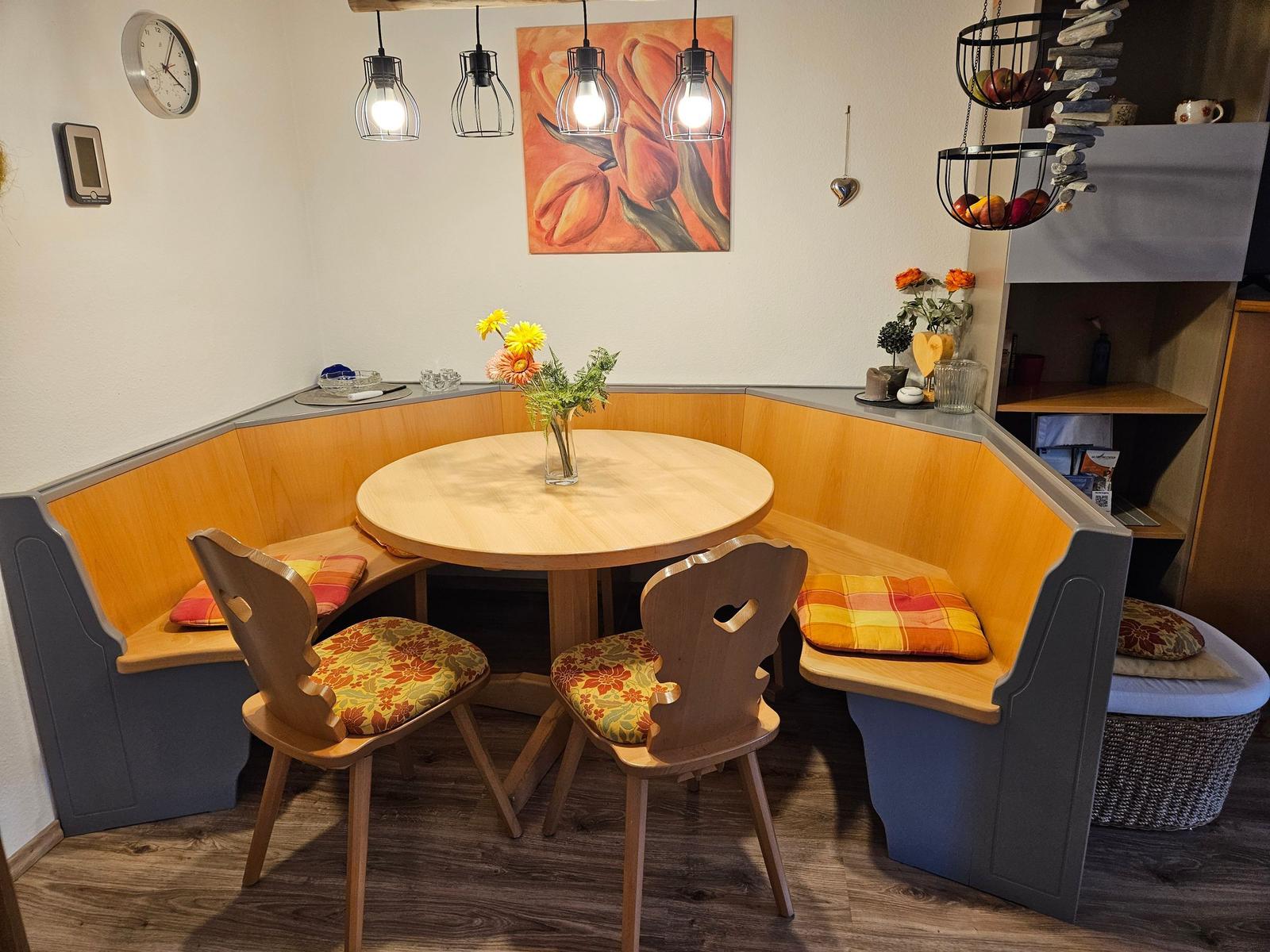 Runder Holztisch mit zwei Stühlen und Sitzbank in Ecke. Wandbild und Hängelampen.