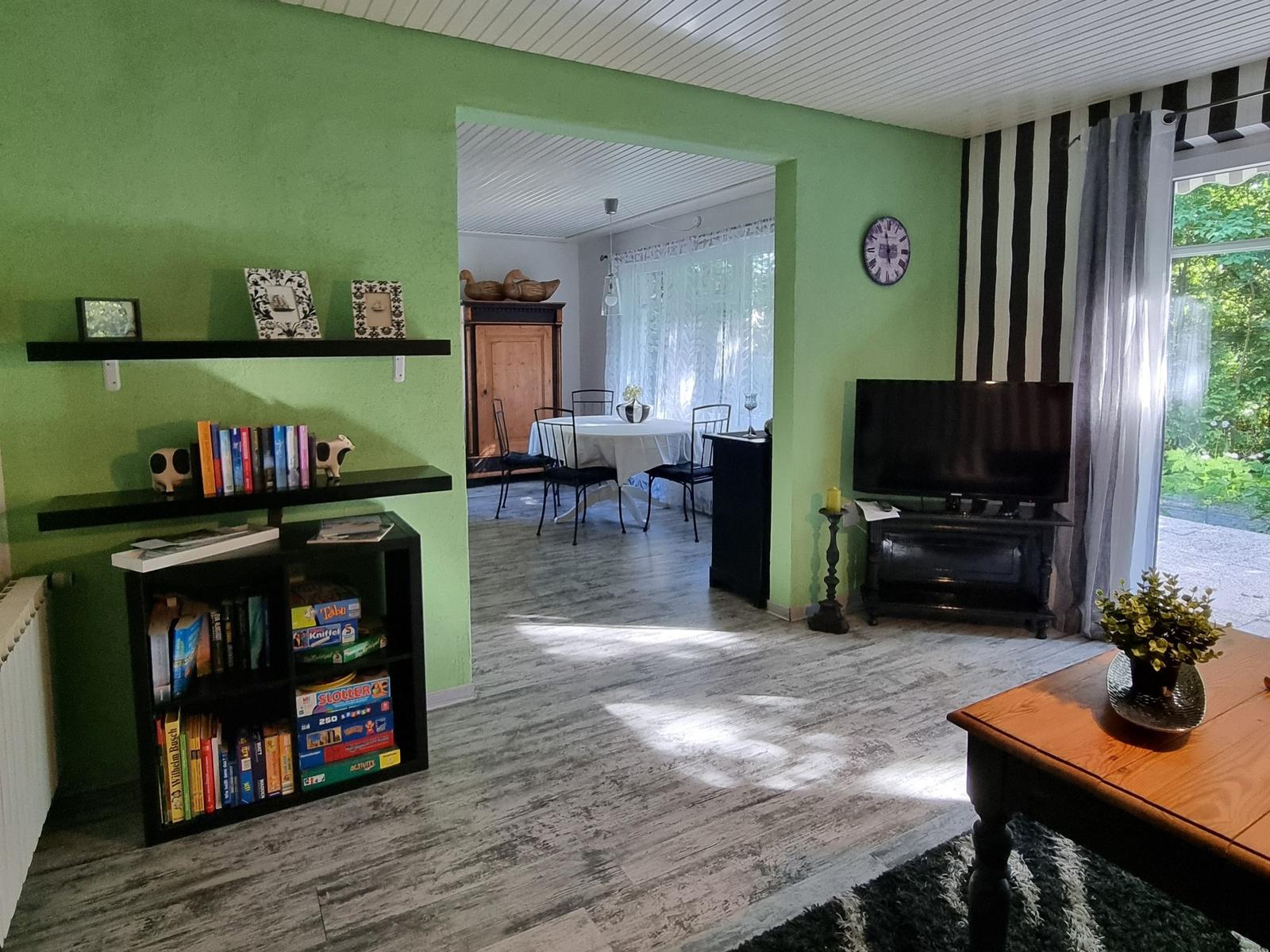 Living room with TV, bookcase, and view into dining room. Green walls and wooden floor.