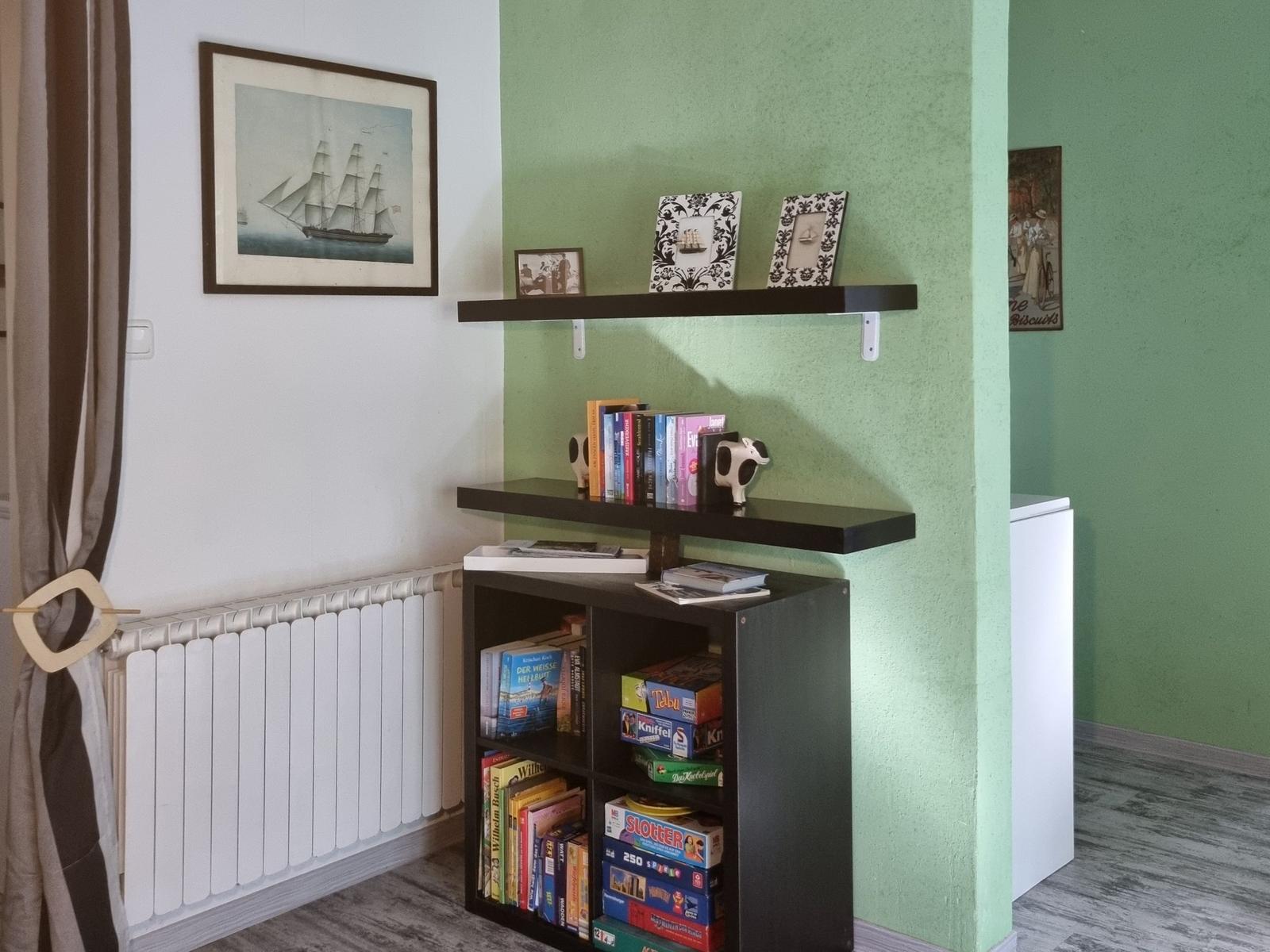 A room with green walls, a bookcase, and wall pictures of ships.
