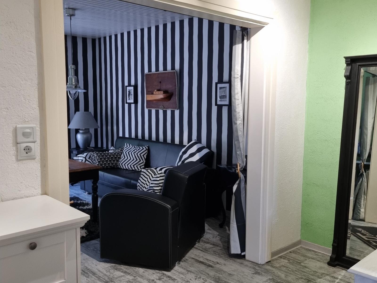 Black sofa with cushions against striped wall. Mirror and wooden table in background.
