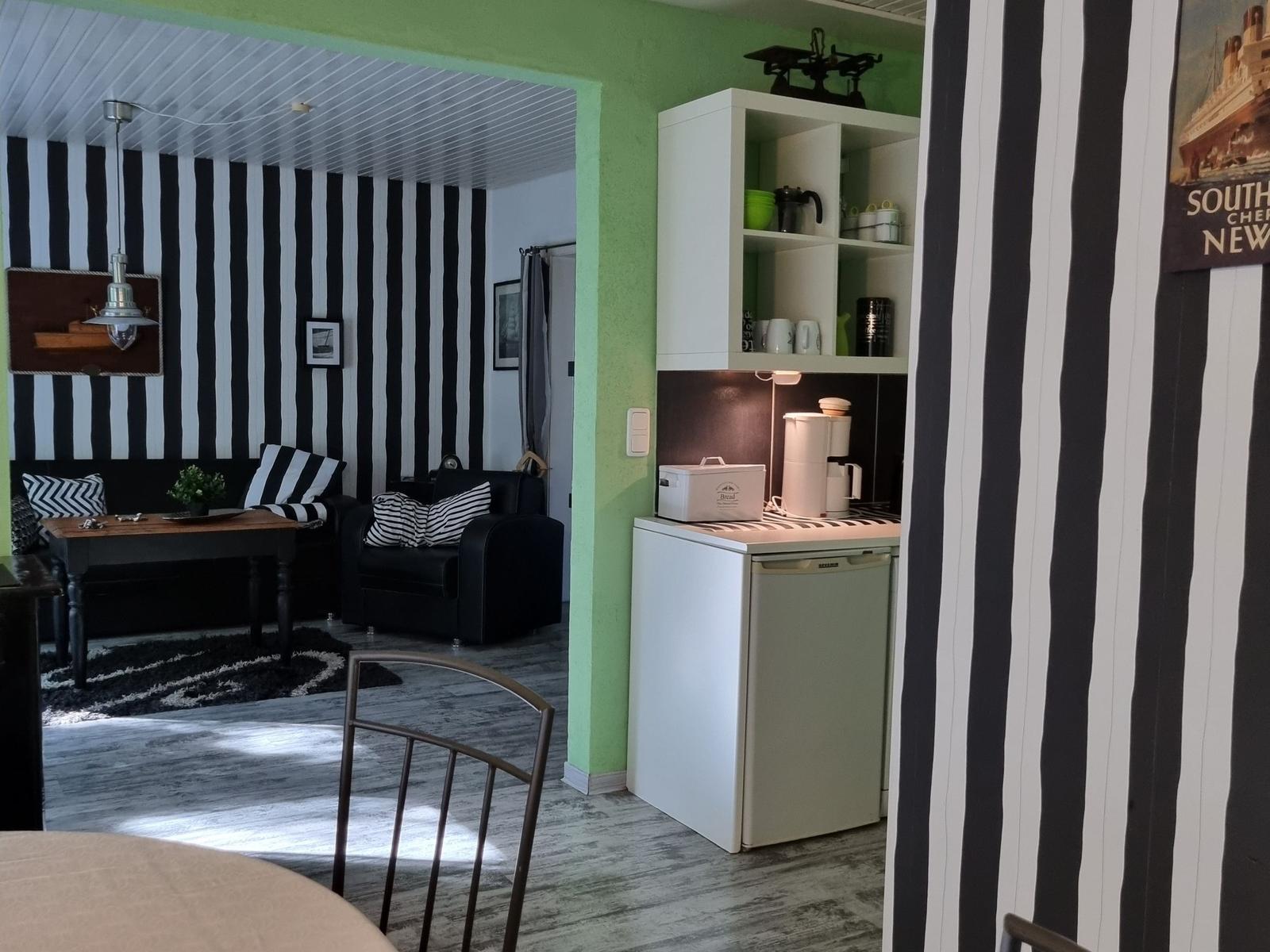 Living area with black-and-white striped wall and small kitchen with refrigerator.