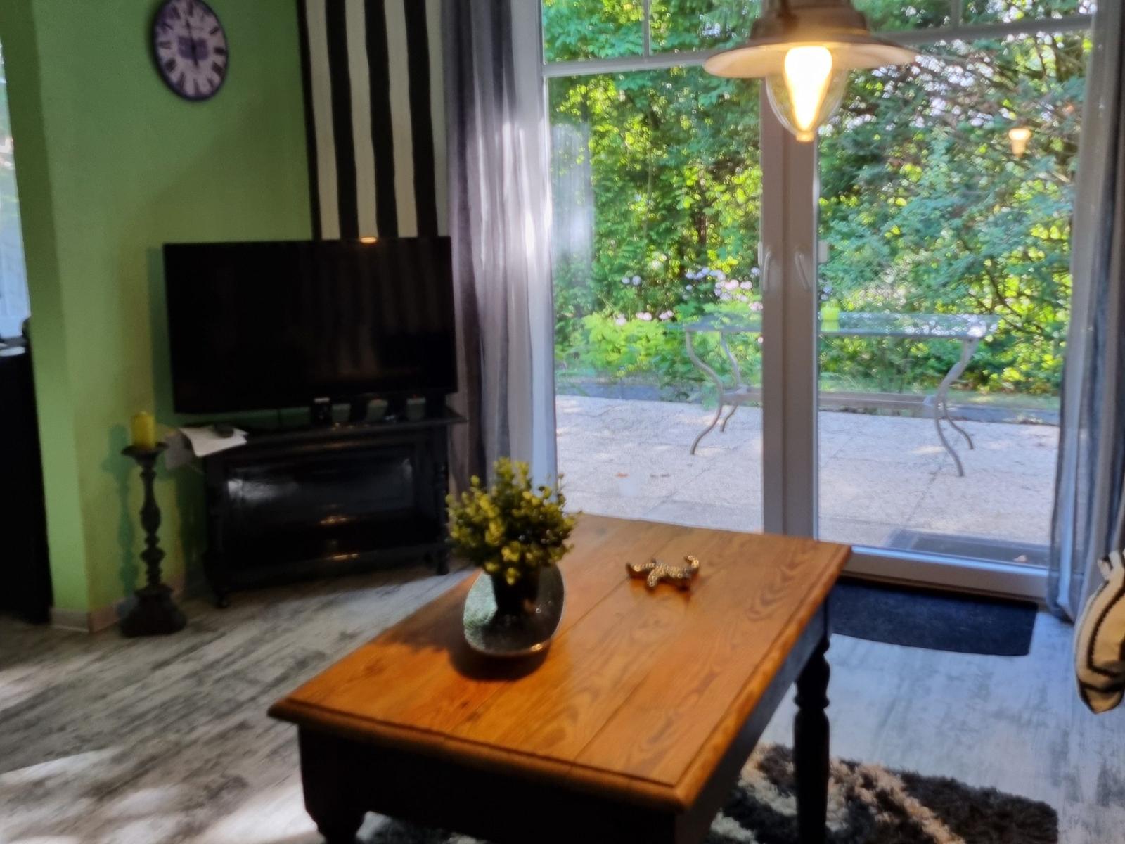 Living room with TV, wooden table, and view of the terrace