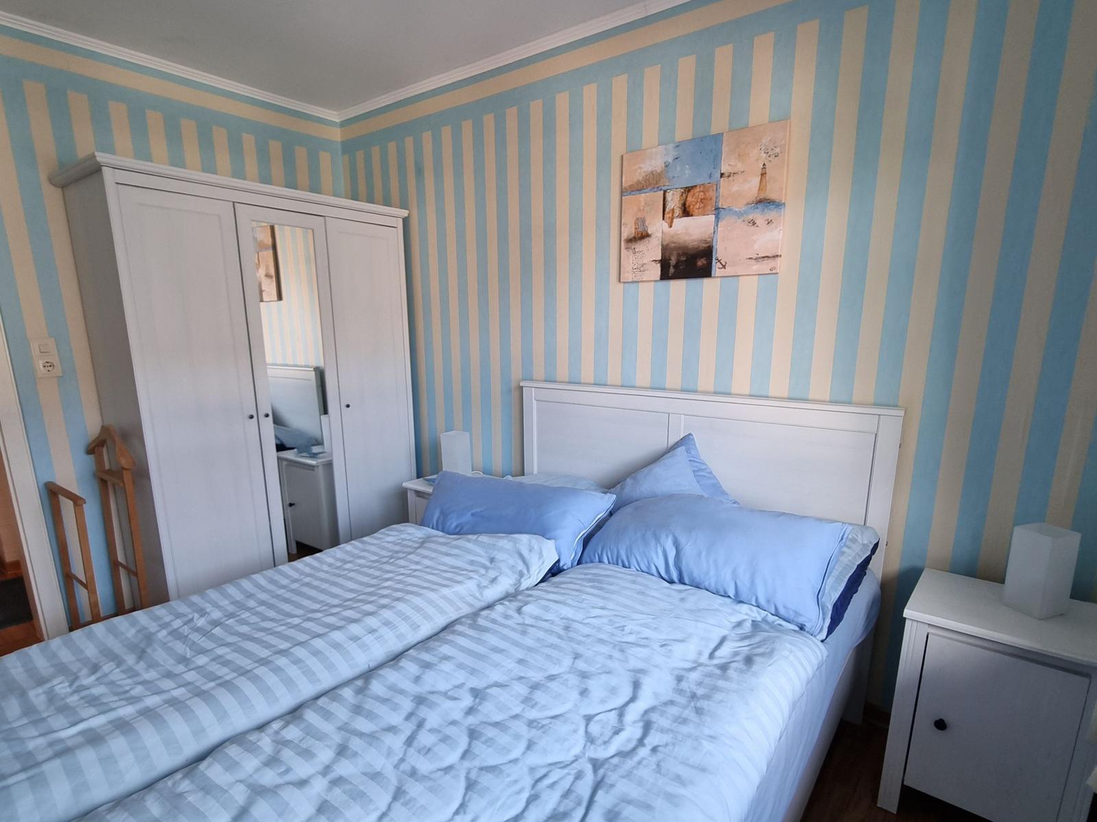 Bedroom with striped walls, white bed, and wardrobe.