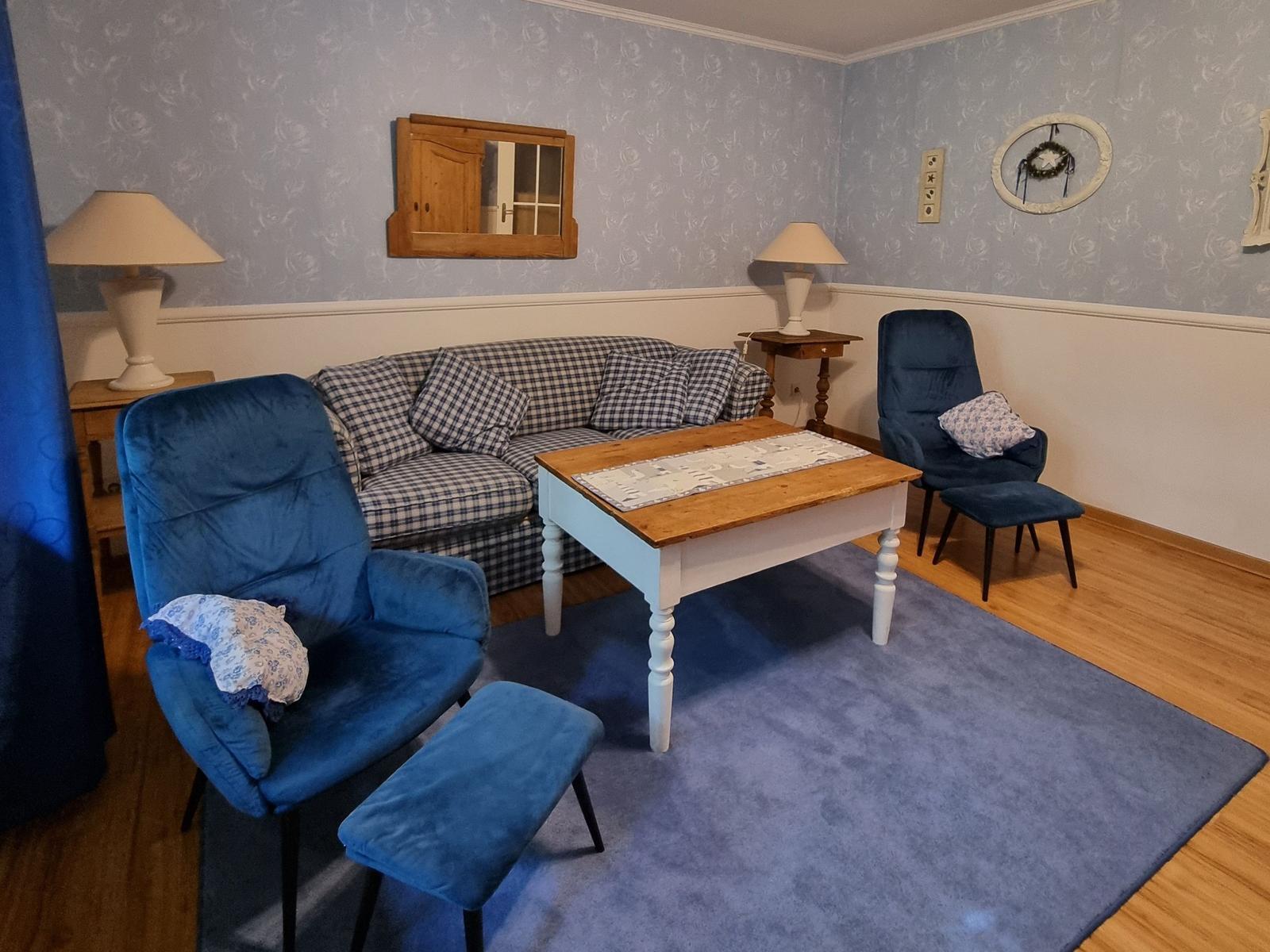 Living room with sofa, two blue chairs, and wooden table on rug.