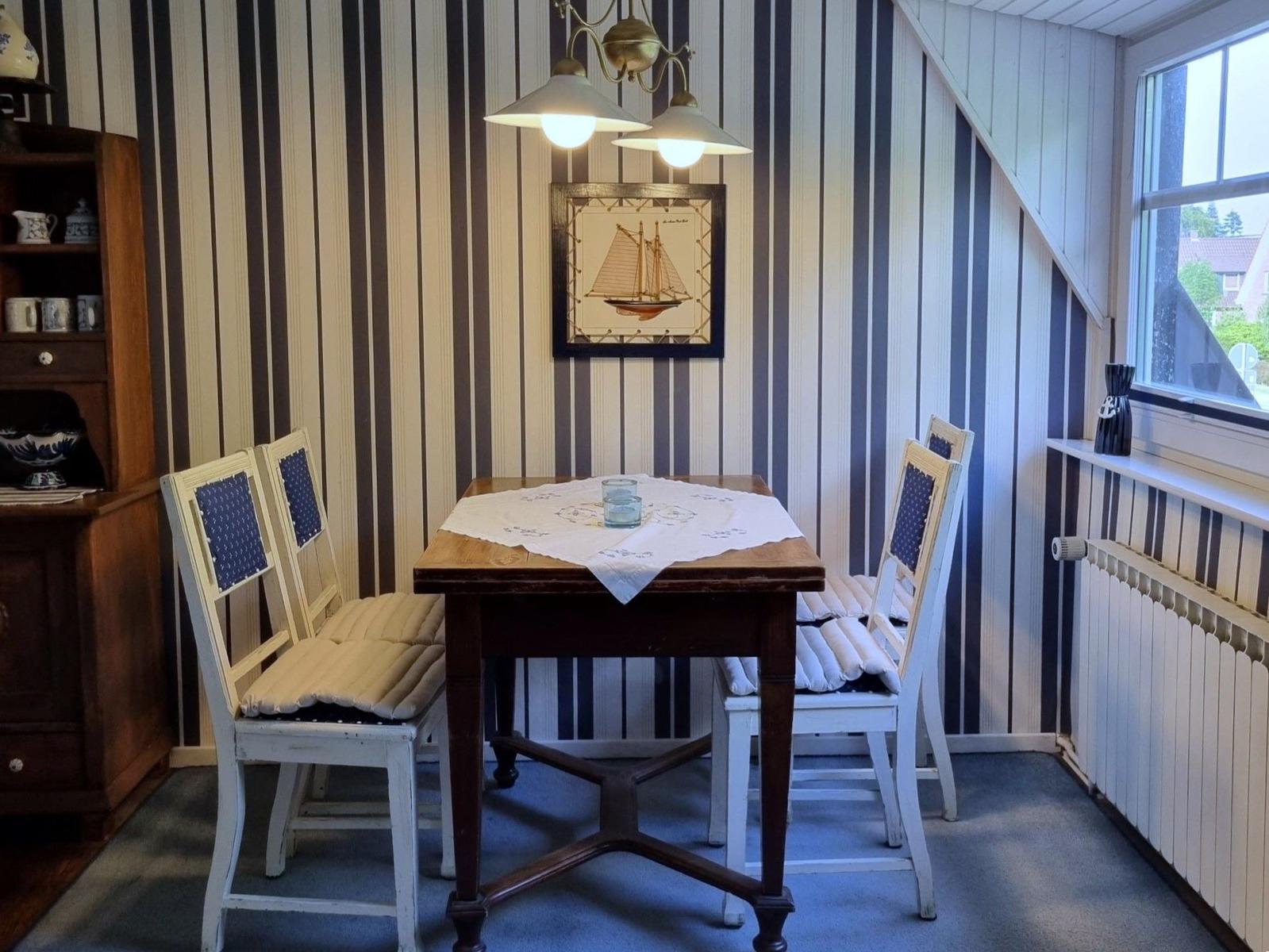 Dining room with wooden table, four chairs, and striped walls. Window and ceiling lights visible.