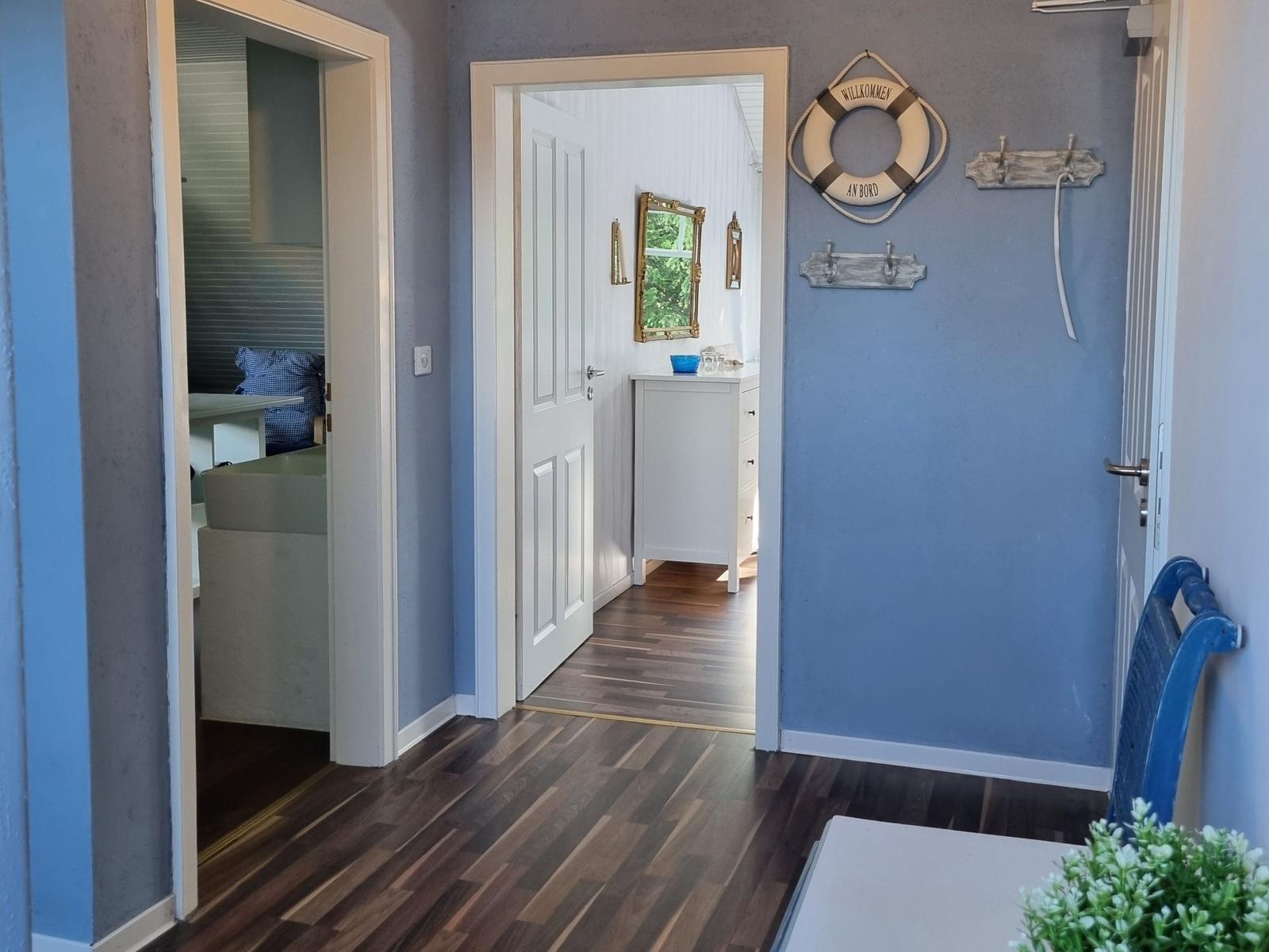 Hallway with blue walls, wooden floor, and nautical decor. Doors lead to bedroom and bathroom.