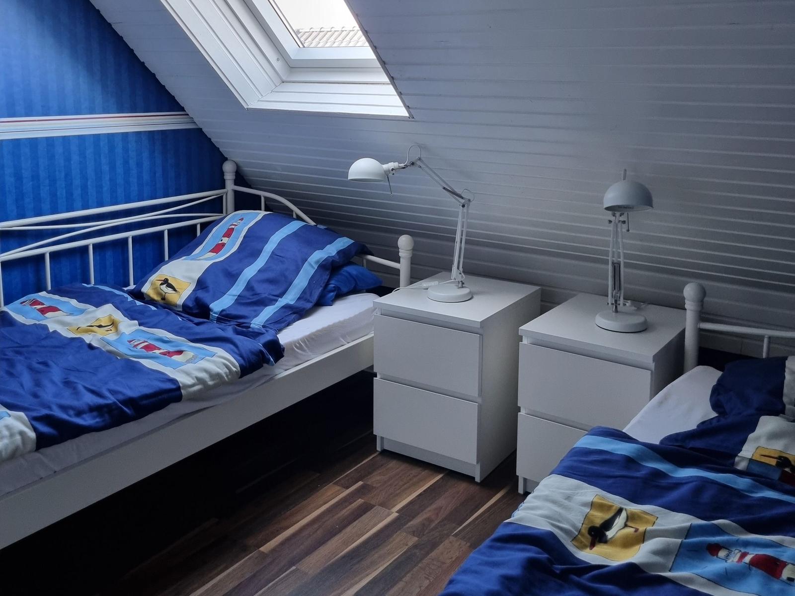 Room with two beds, nightstands, and skylight. Blue bedding with lighthouse motif.