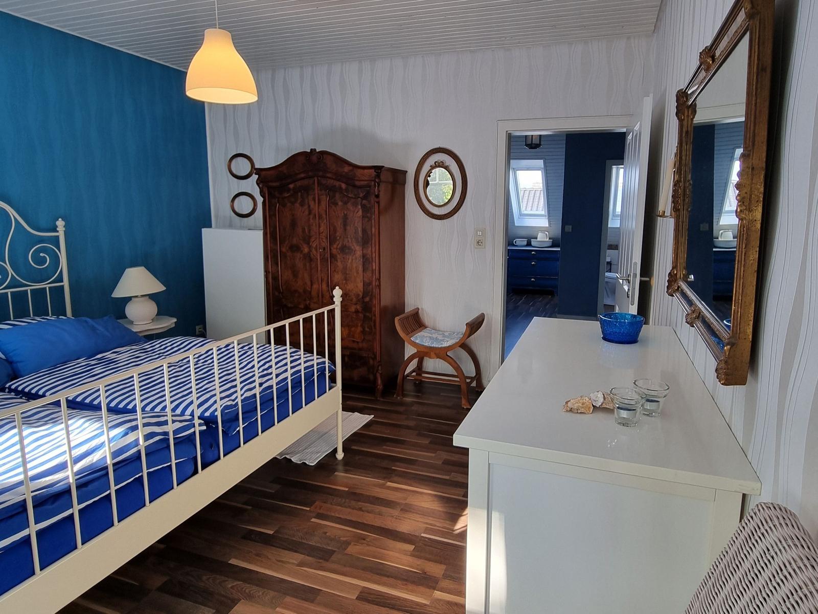 Bedroom with bed, wardrobe, and mirror. View into bathroom with shower.