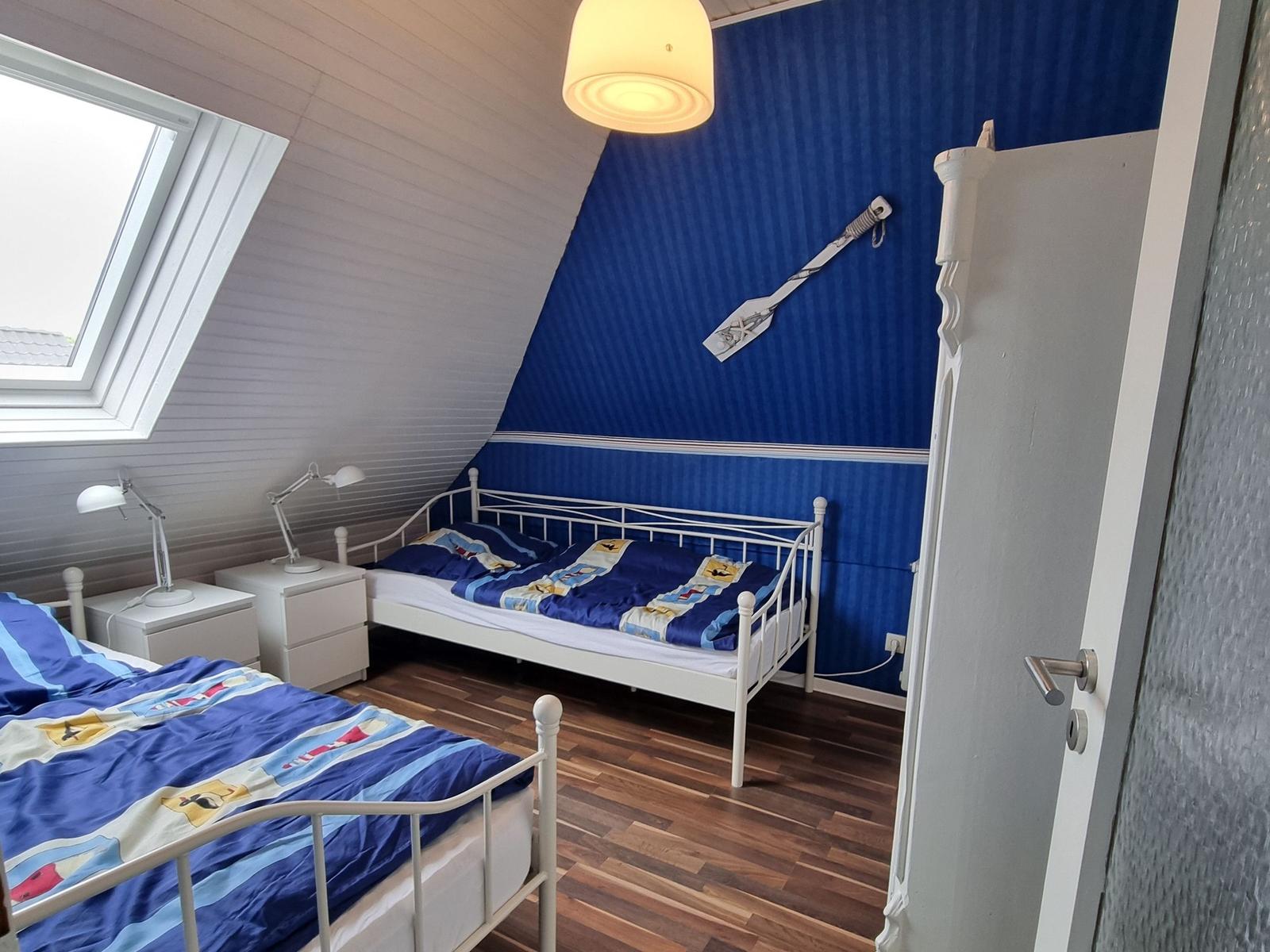 Room with two beds, blue wall, and skylight.