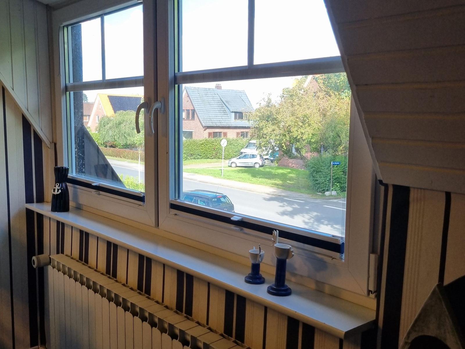 View of street with cars and houses. Windowsill with black vases and cups.
