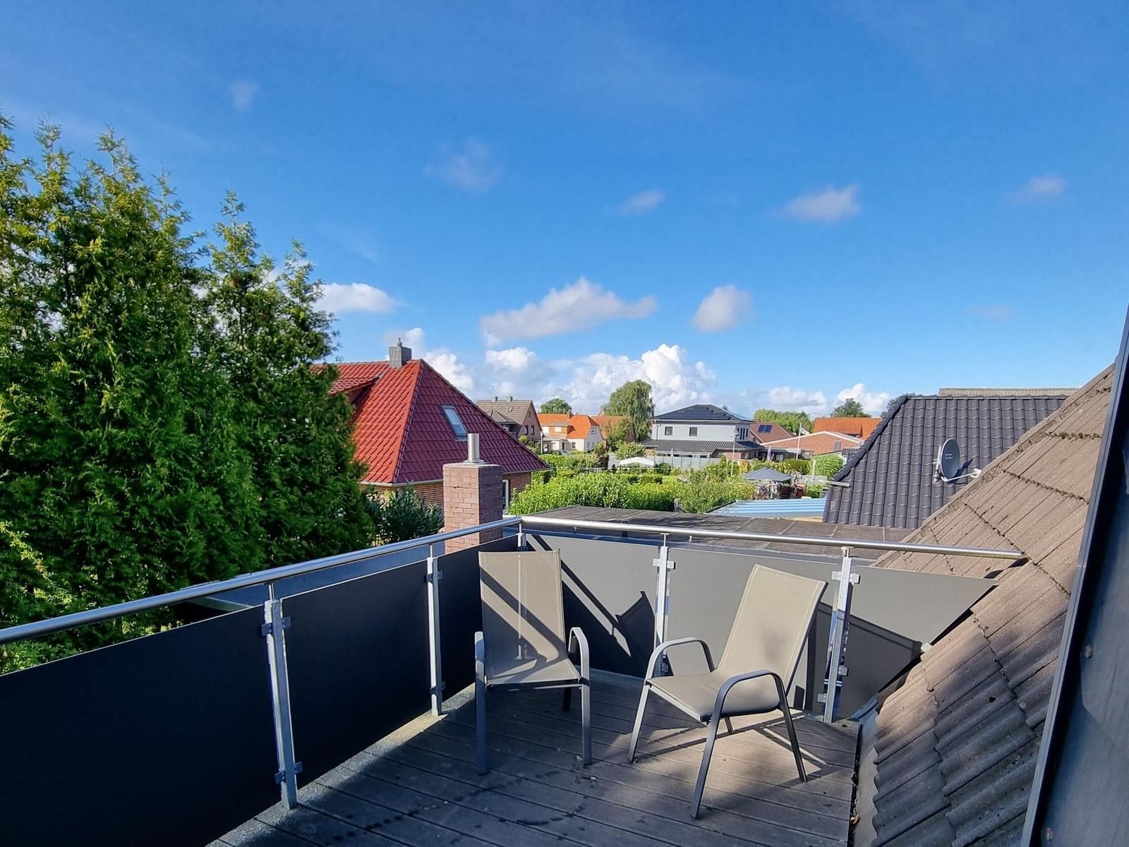 Terrace with two lounge chairs and view of rooftops and trees under blue sky.