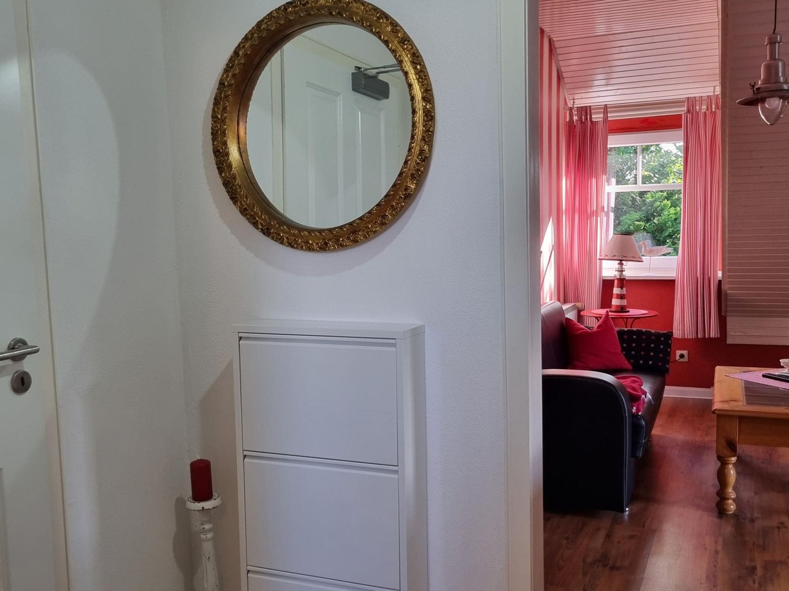 Entryway with mirror and cabinet. View into living room with sofa and window.