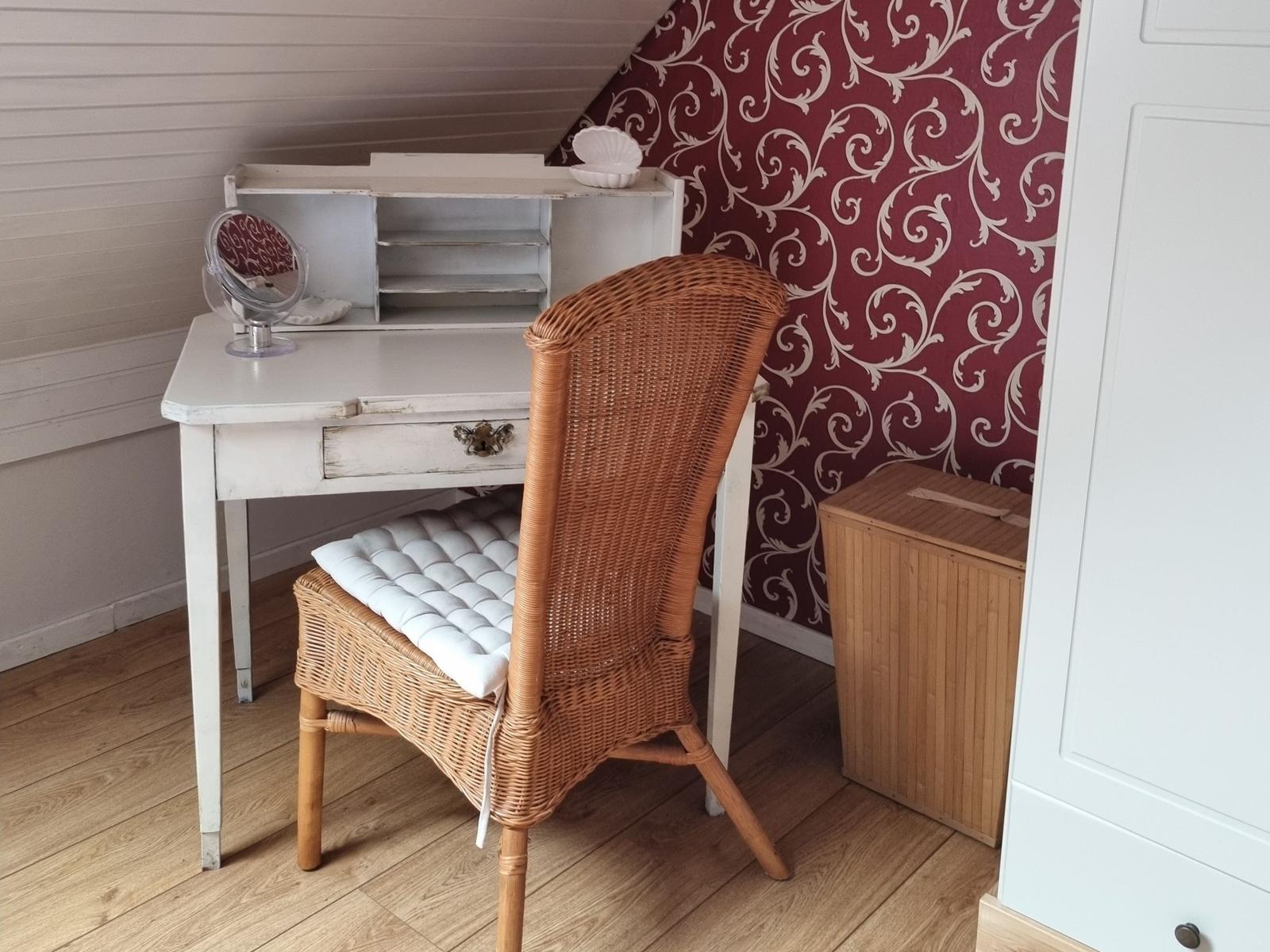 Desk with chair, wallpapered wall, wooden floor, and closet in room.